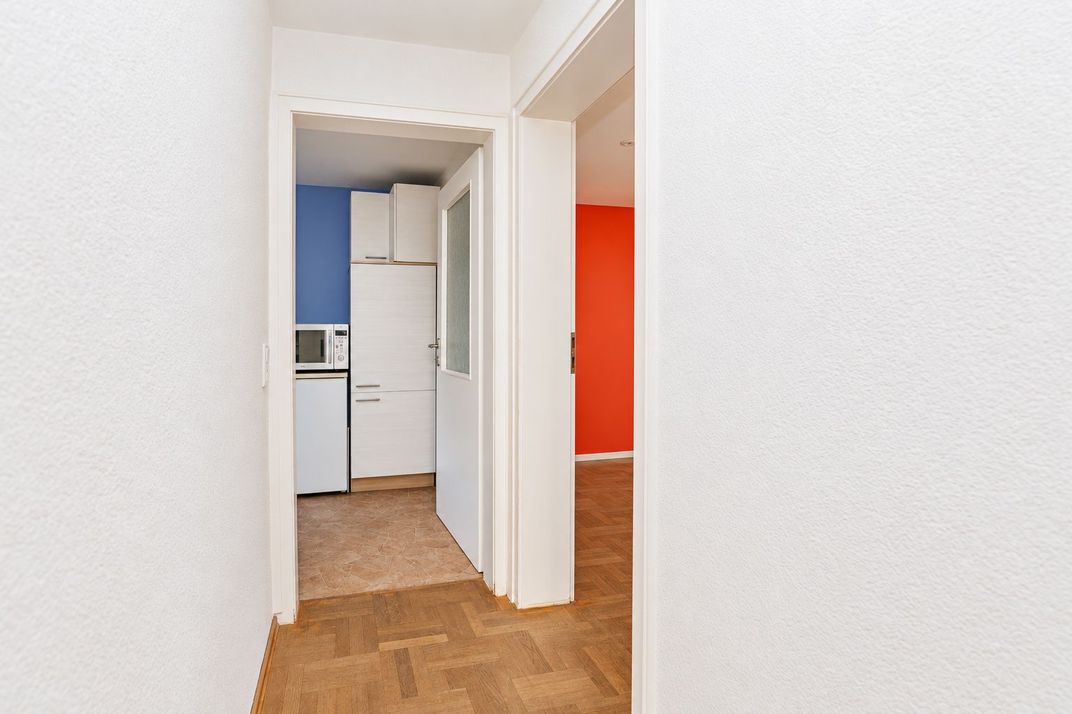 Flur mit Blick in eine weiße Küche und ein Zimmer mit roter Wand.