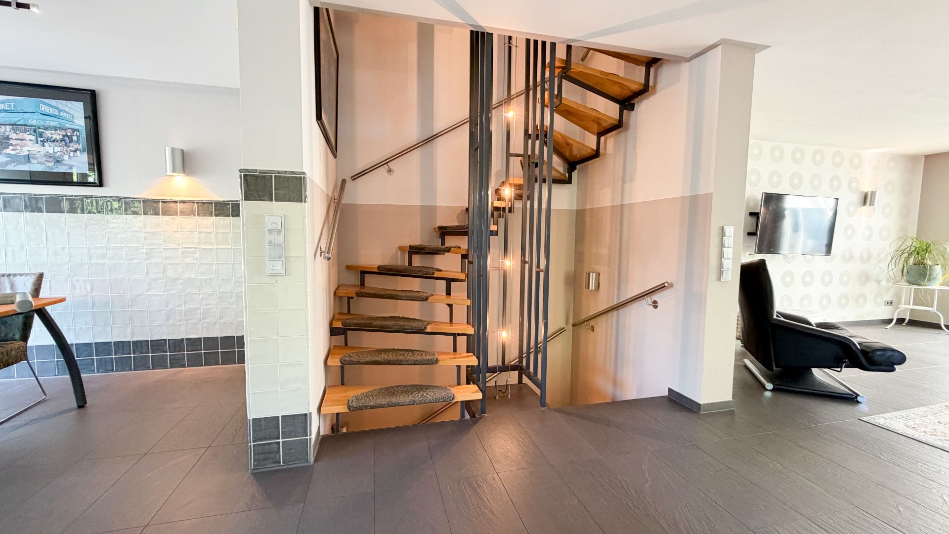 Helles Wohnzimmer mit moderner Holztreppe und Sessel, Fernseher an der Wand.