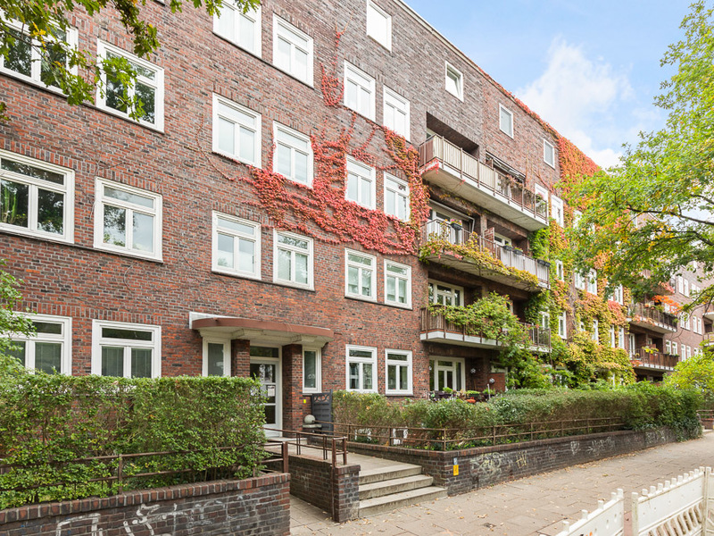 Mehrstöckiges Wohnhaus mit roten Klinkersteinen, Balkonen und Kletterpflanzen an der Fassade.