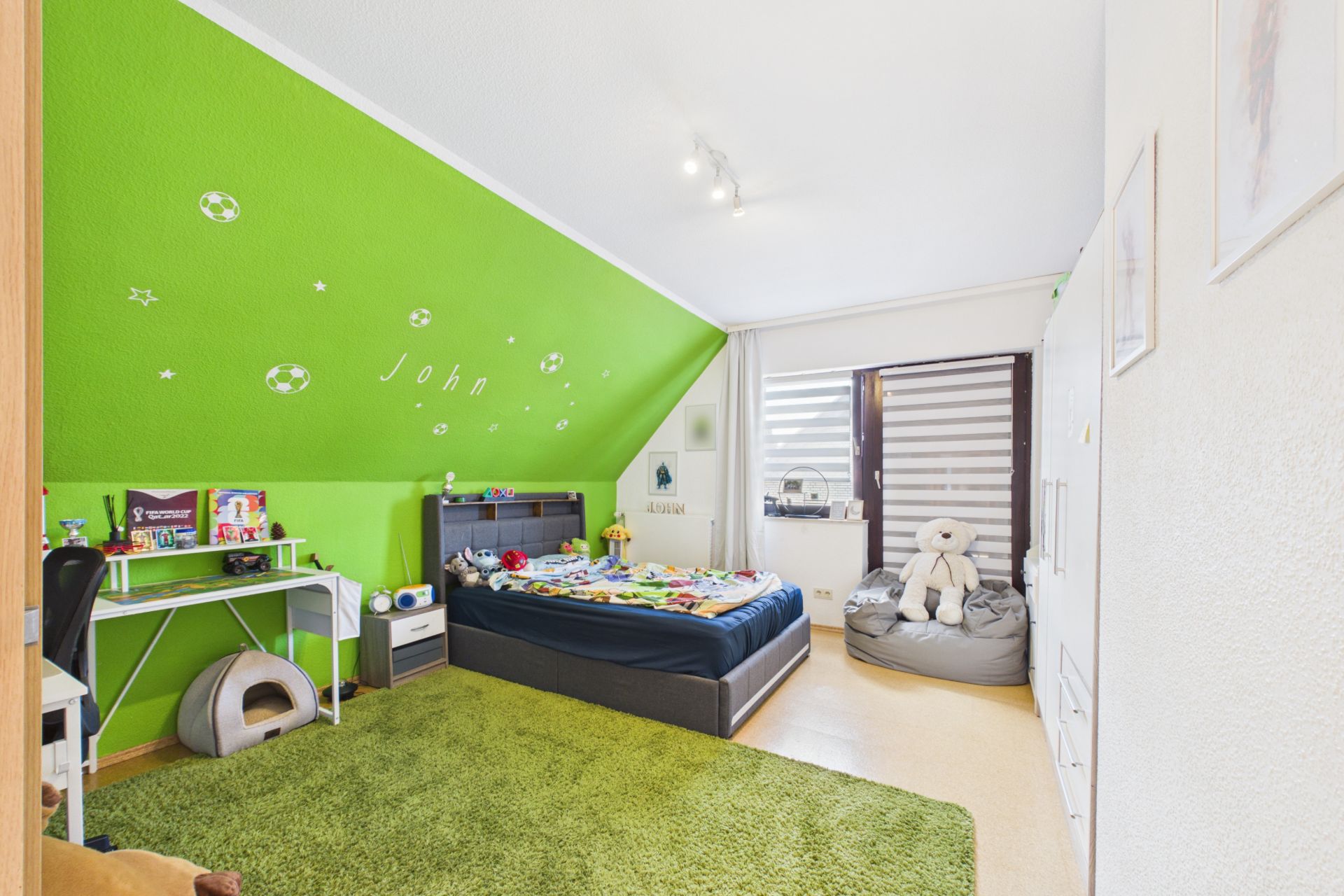 Helles Kinderzimmer mit grün gestrichener Wand, Bett, Schreibtisch und großem Teppich.