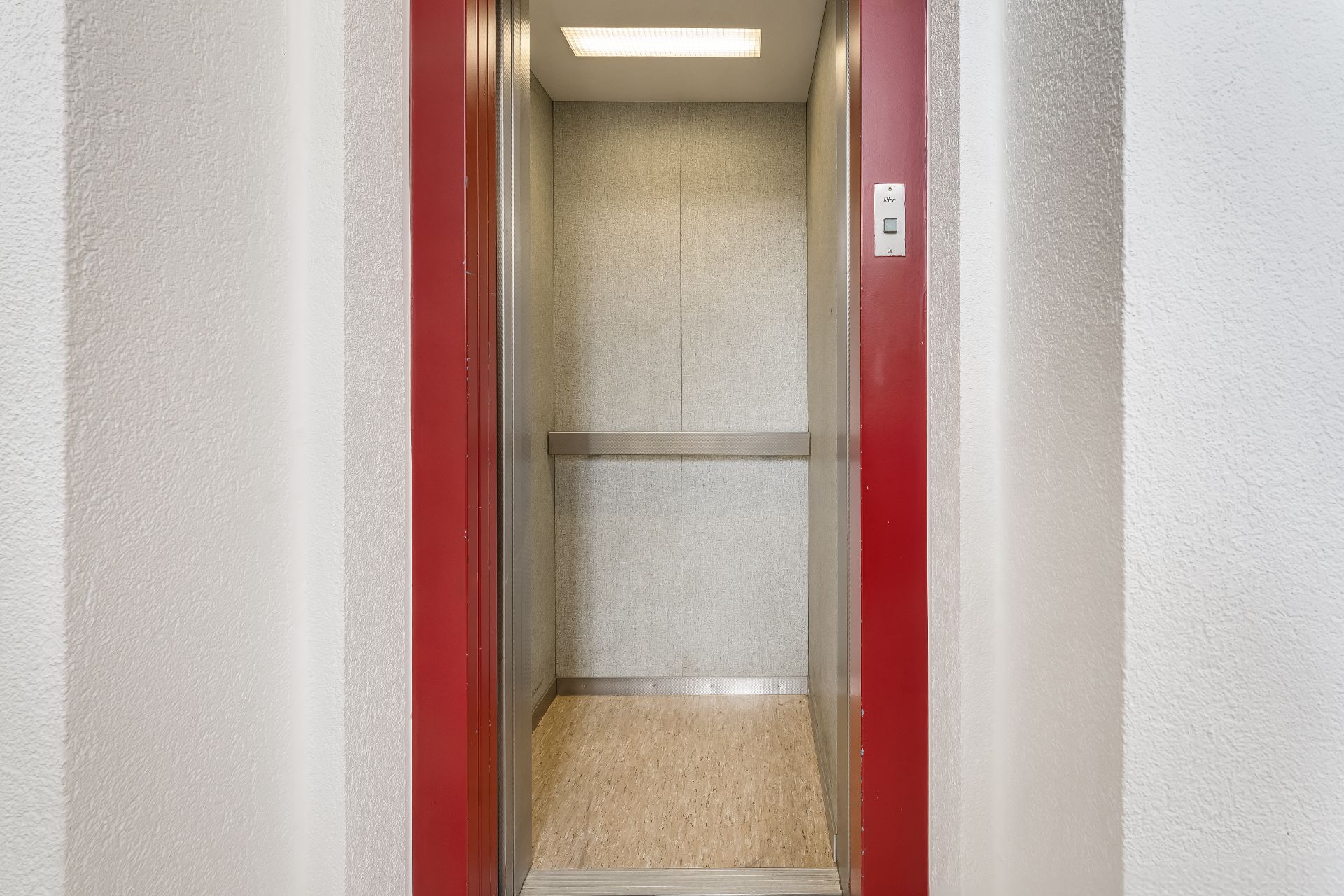 Geöffneter Aufzug mit roten Türrahmen und hellem Innenraum in einem Wohngebäude.