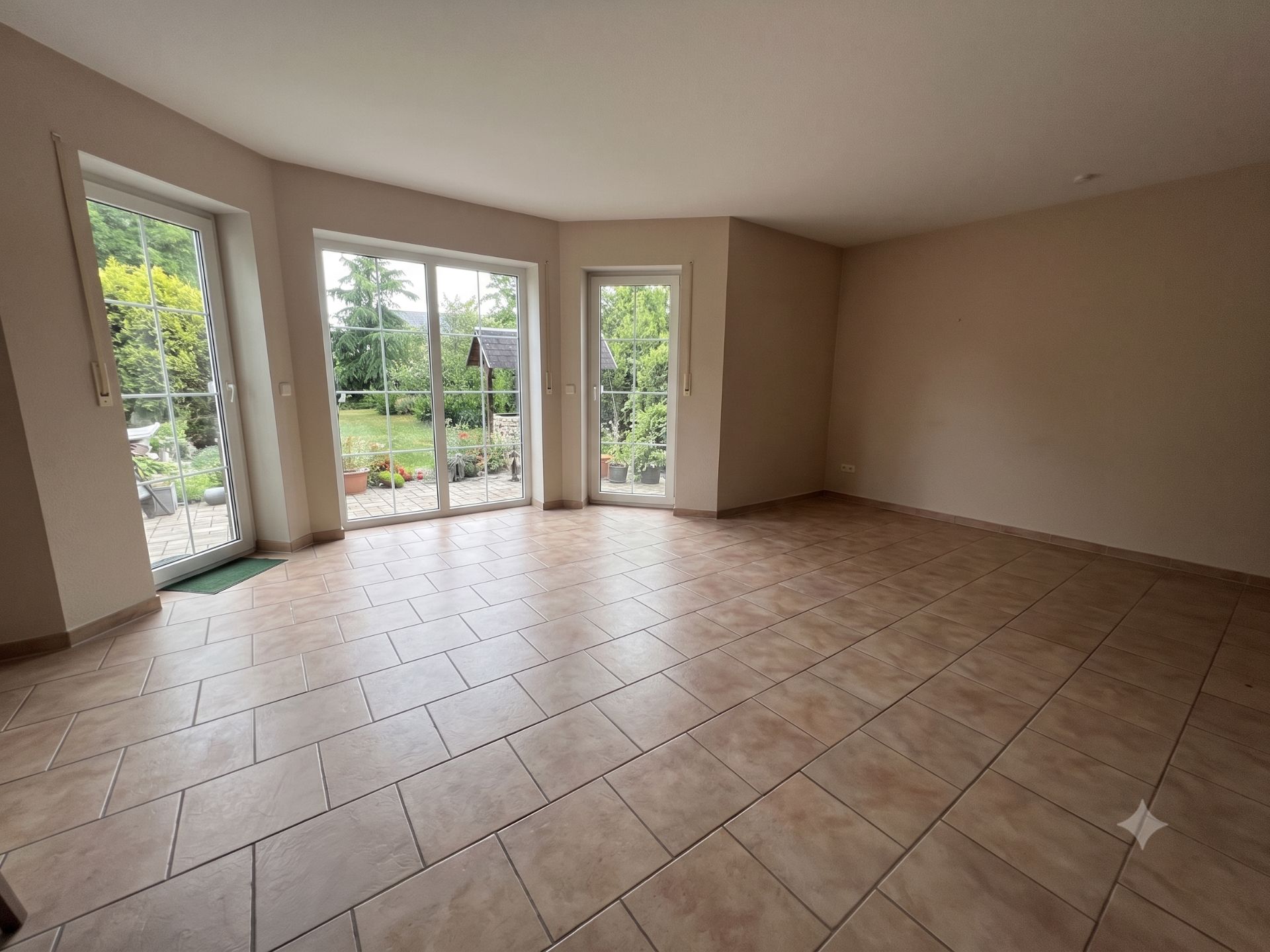 Leerer, gefliester Raum mit großen Fenstern und Blick auf einen Garten.