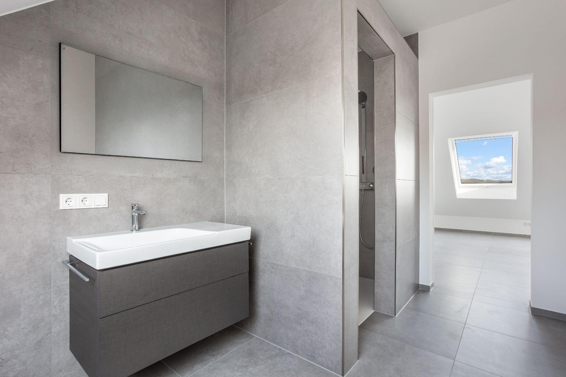 Modernes Badezimmer mit Waschbecken, Spiegel und begehbarer Dusche, angrenzend an einen hellen Raum.