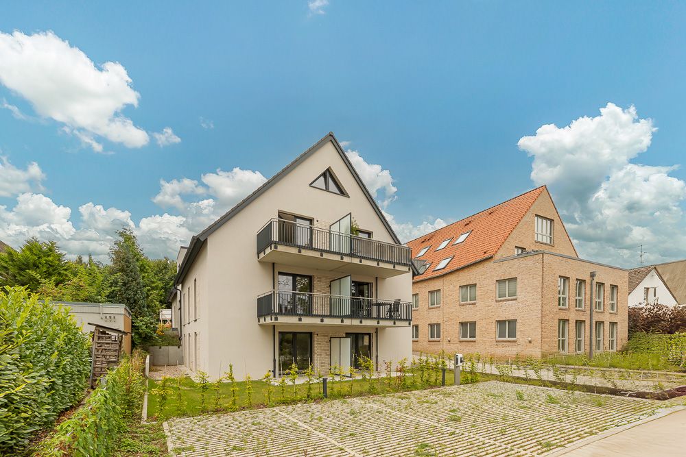 Modernes Wohngebäude mit Balkonen und Parkplatz davor, daneben ein weiteres Wohnhaus.