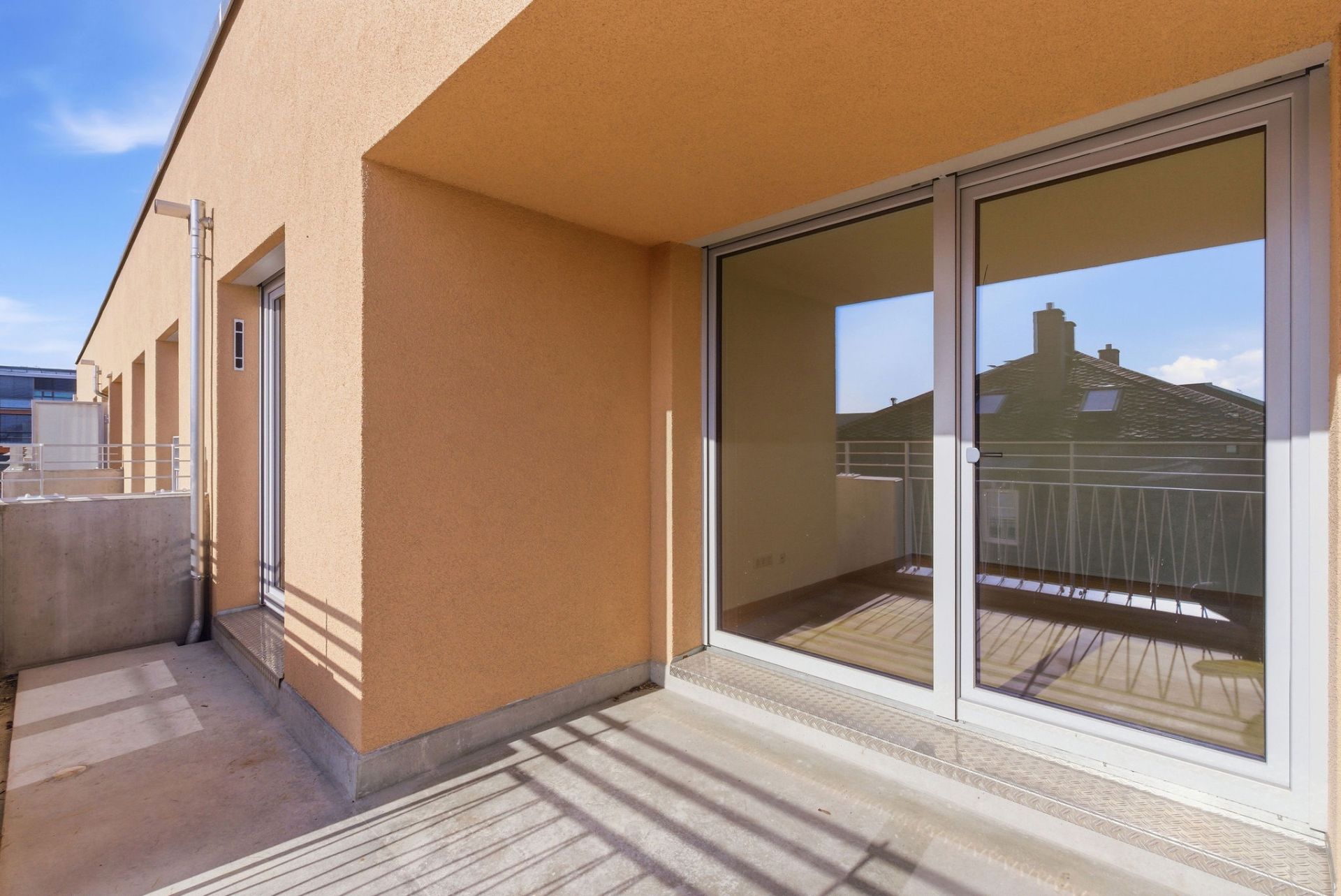Großer Balkon mit Glas-Schiebetüren und Geländer an einem Wohngebäude.