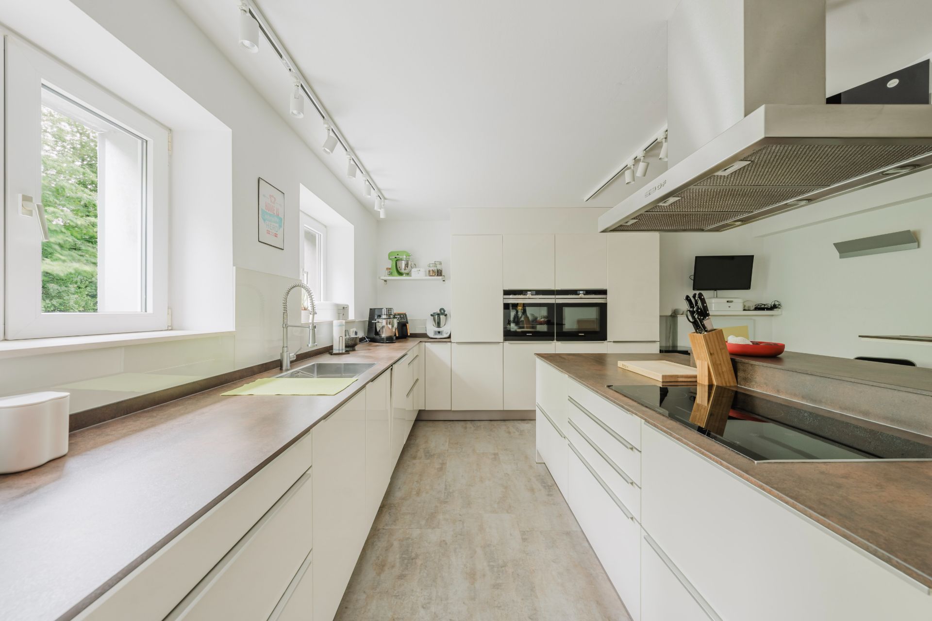 Helle, moderne Küche mit weißen Schränken, großem Fenster und Einbaugeräten.