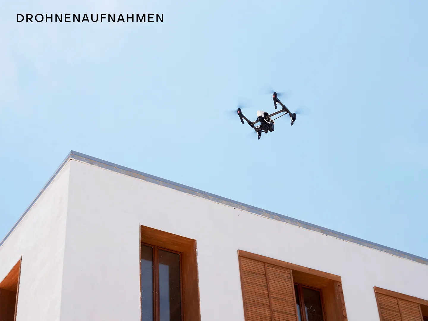 Eine Drohne fliegt über das Dach eines modernen Wohnhauses mit Holzfenstern.