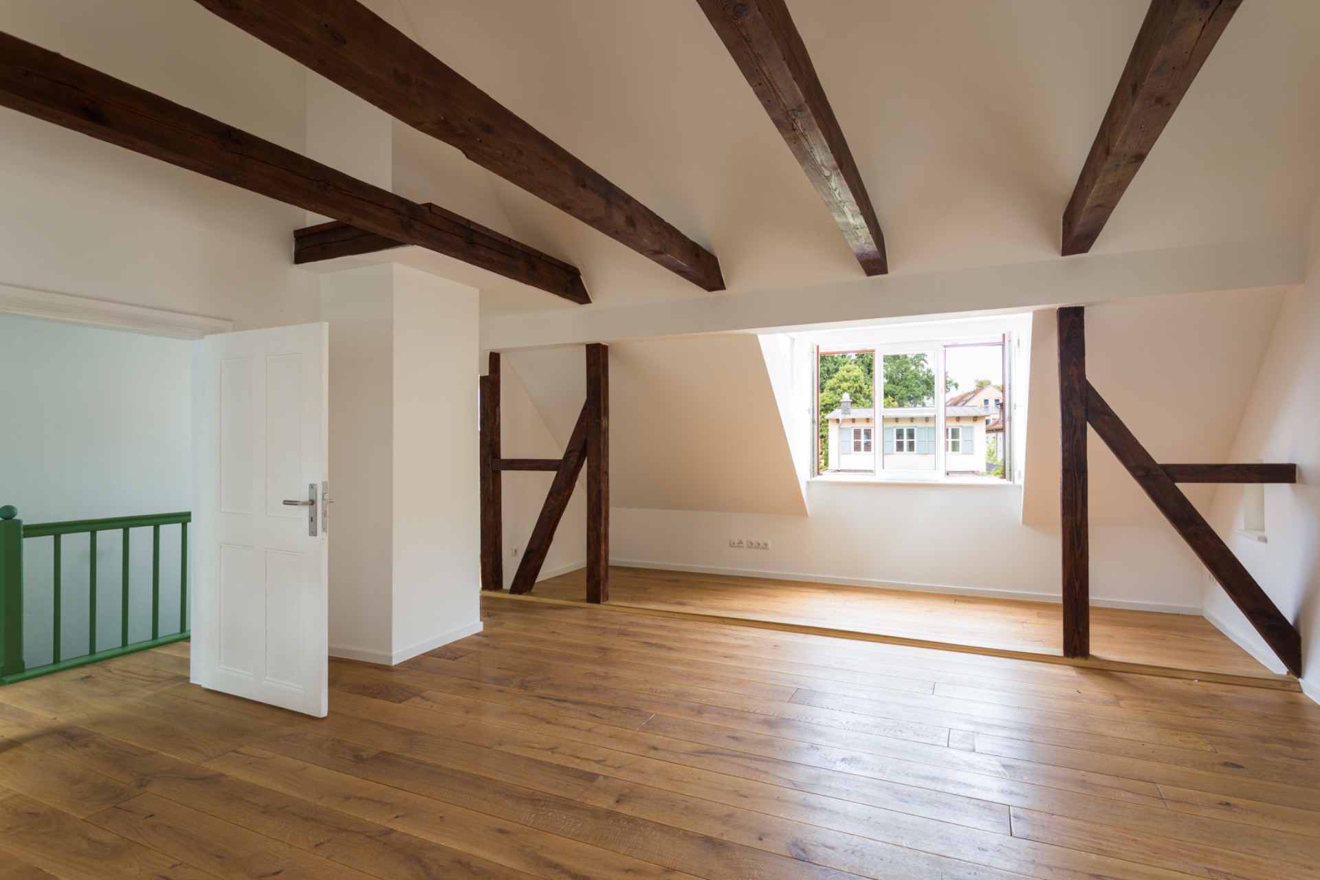 Heller Raum mit Holzbalken, Holzboden und offenem Fenster, grünem Geländer und weißen Wänden.