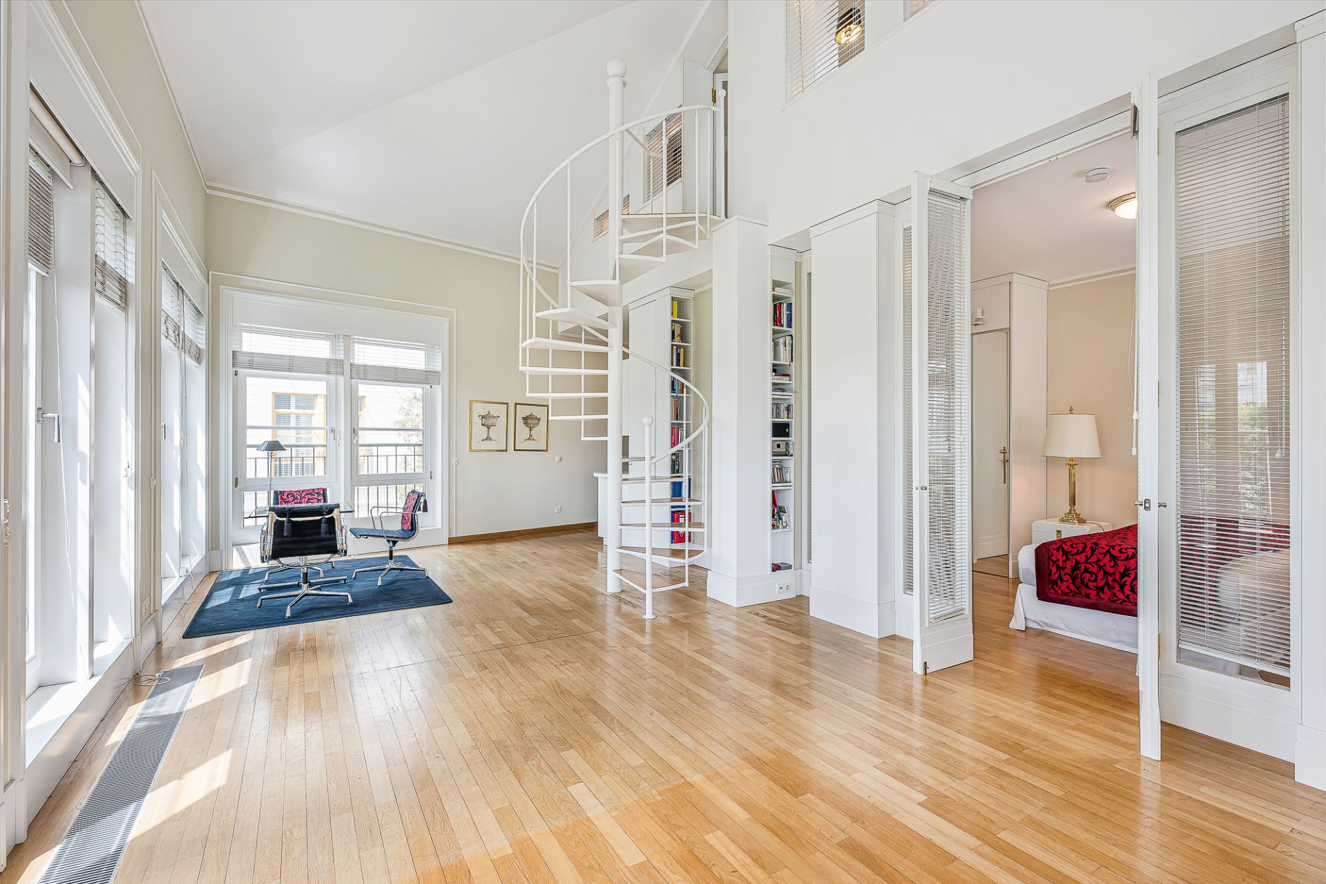 Helles Wohnzimmer mit Holzboden, Wendeltreppe, Schreibtisch und Einblick ins Schlafzimmer.
