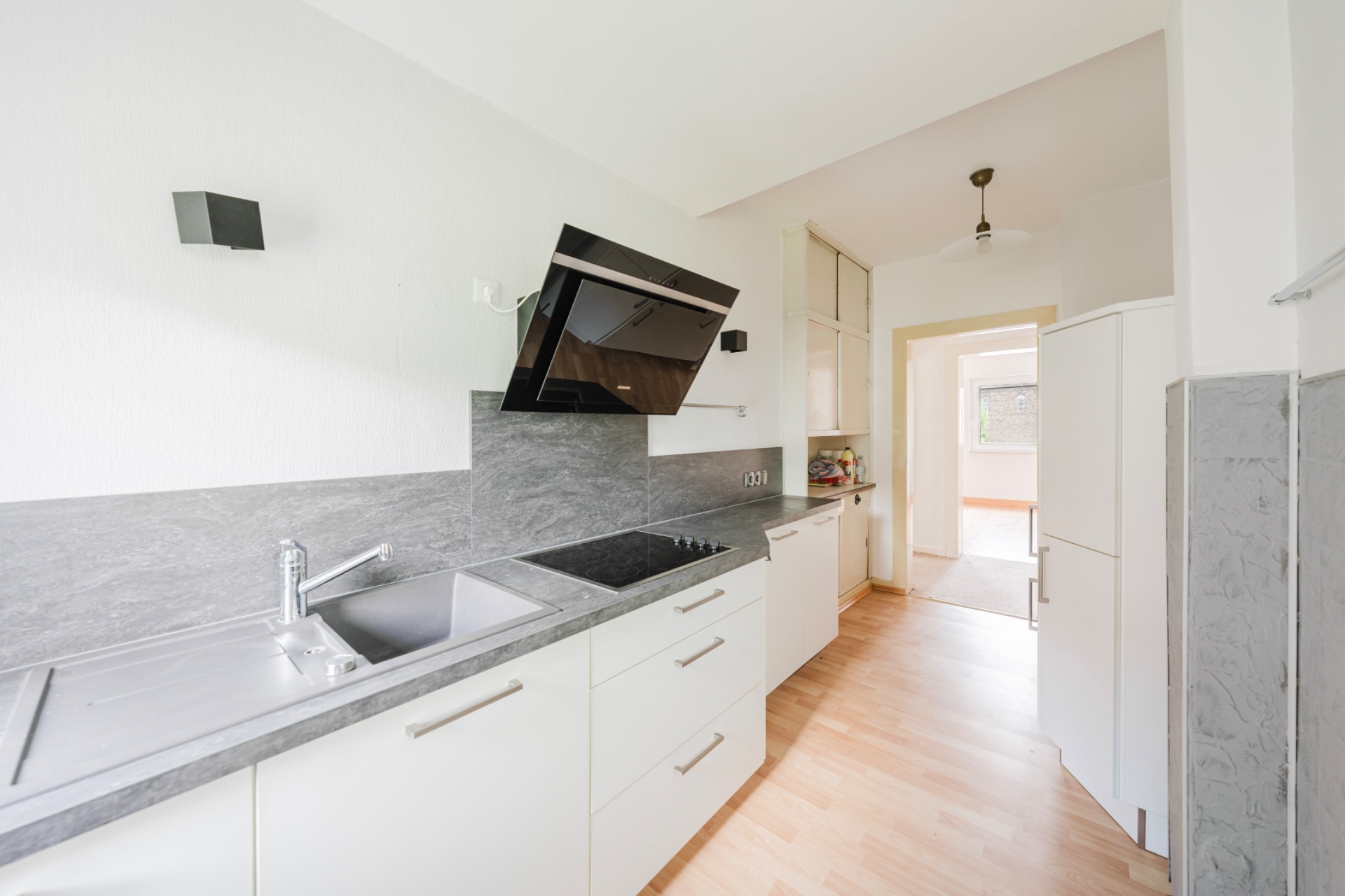 Moderne, helle Einbauküche mit Herd, Spüle und Dunstabzugshaube, Blick in angrenzenden Raum.