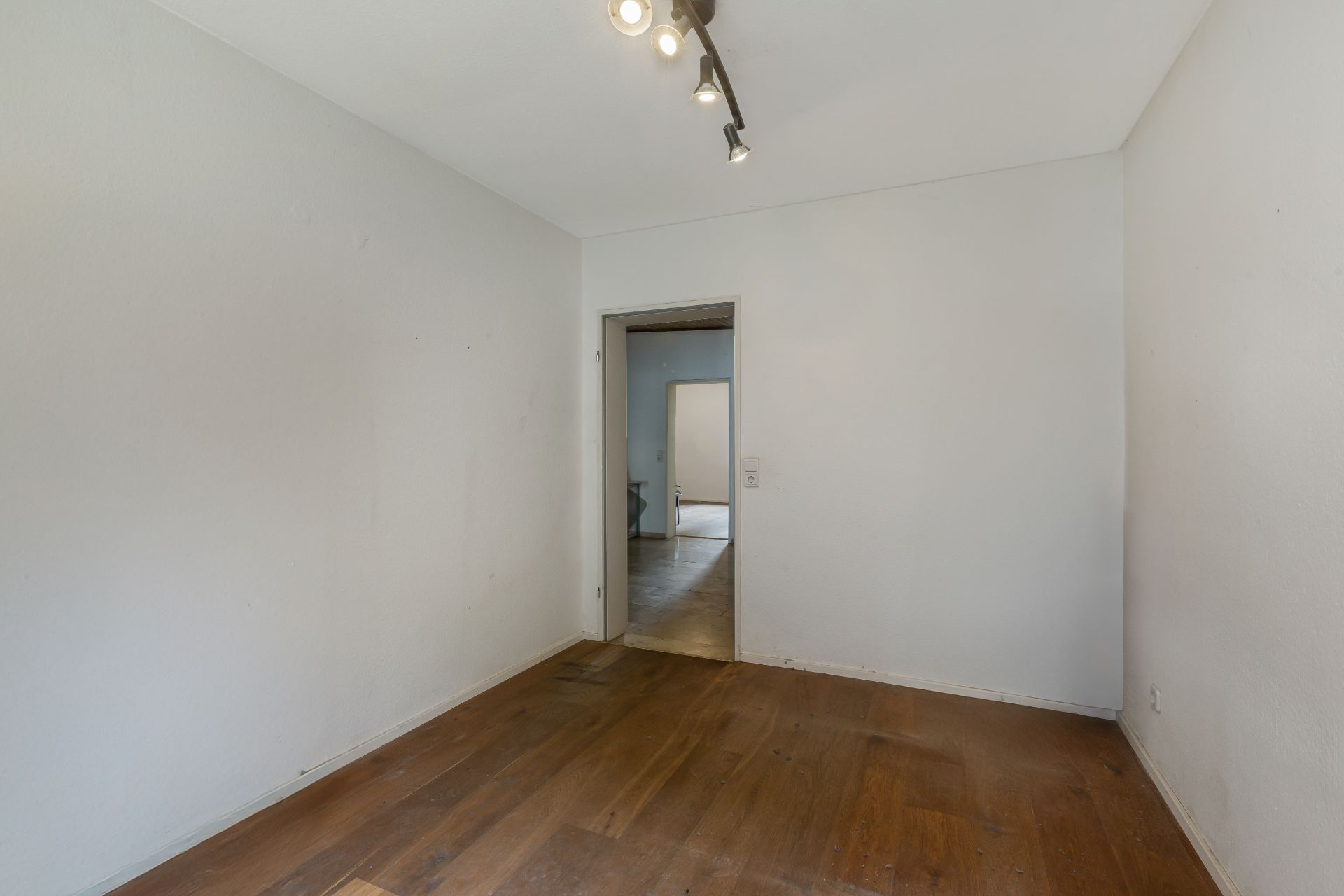 Leerer Raum mit weiß gestrichenen Wänden, Holzfußboden und Deckenlampe.