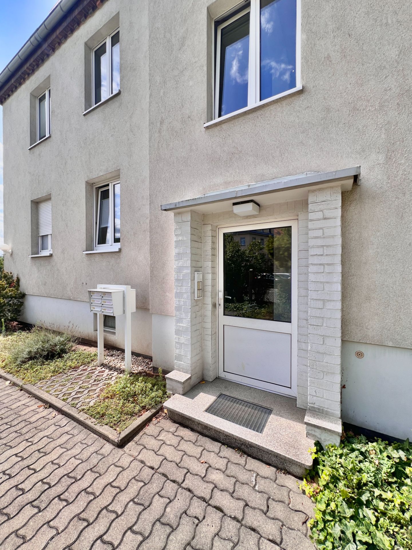 Eingangstür eines Mehrfamilienhauses mit Briefkästen und bepflanztem Bereich davor.