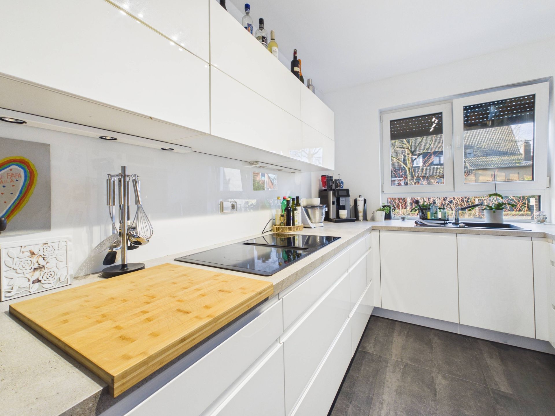 Moderne, helle Küche mit weißen Hochglanzschränken, Fenster und Küchenutensilien.