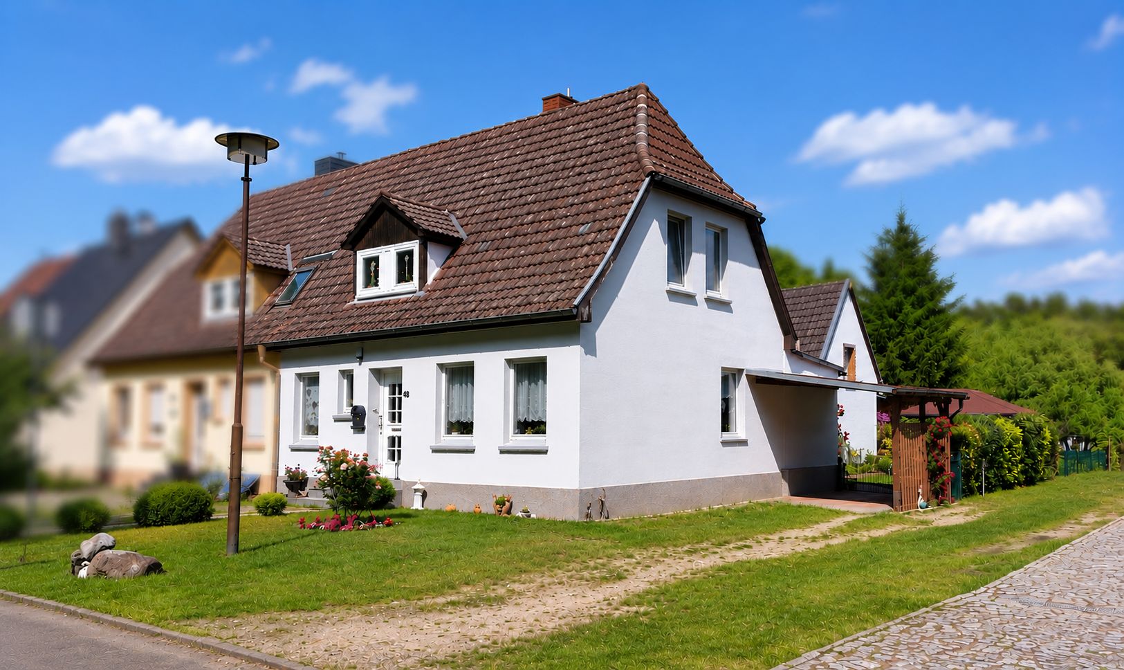 Weißes Einfamilienhaus mit Garten und gepflastertem Weg bei sonnigem Wetter.