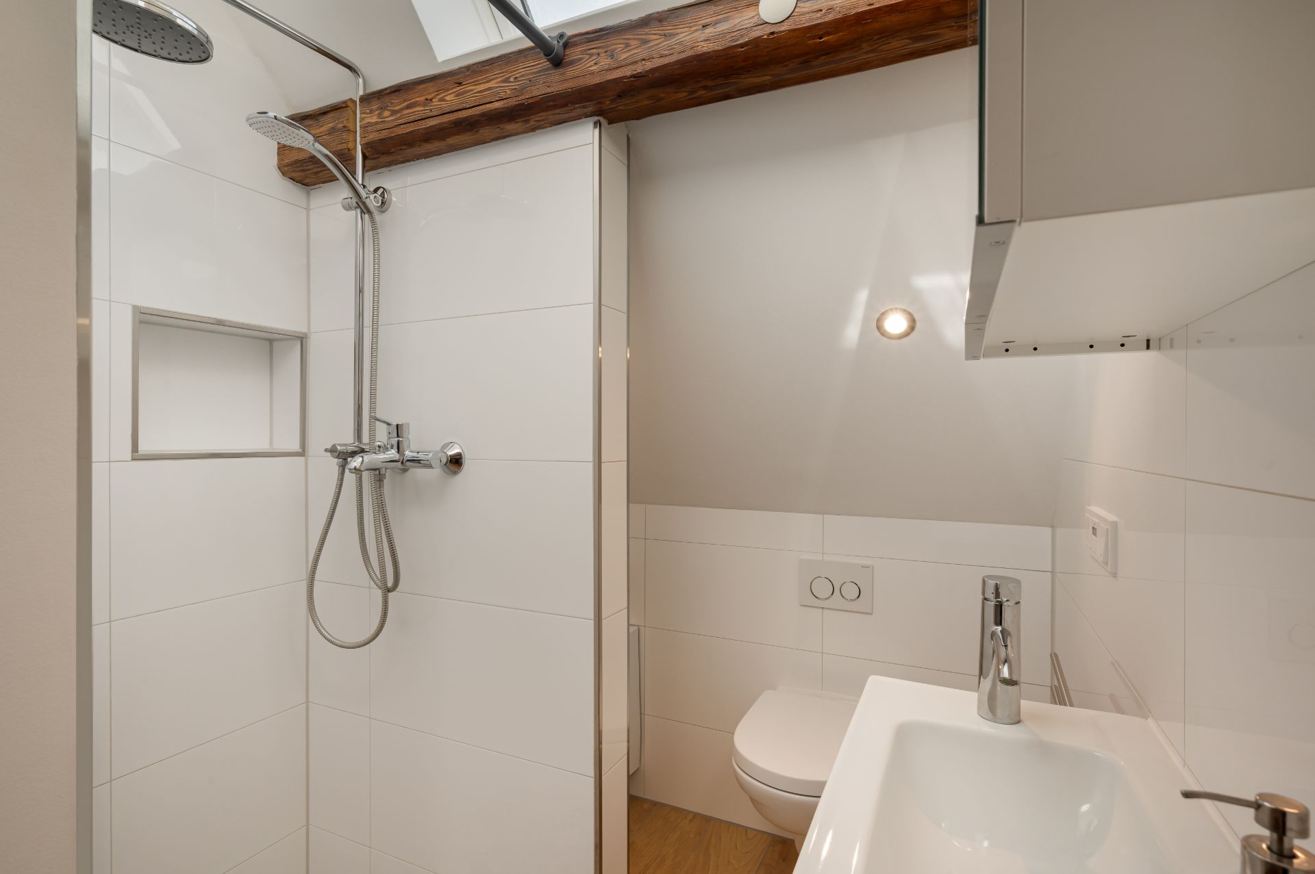 Modernes, kleines Bad mit Dusche, WC und Waschbecken unter einer Dachschräge.