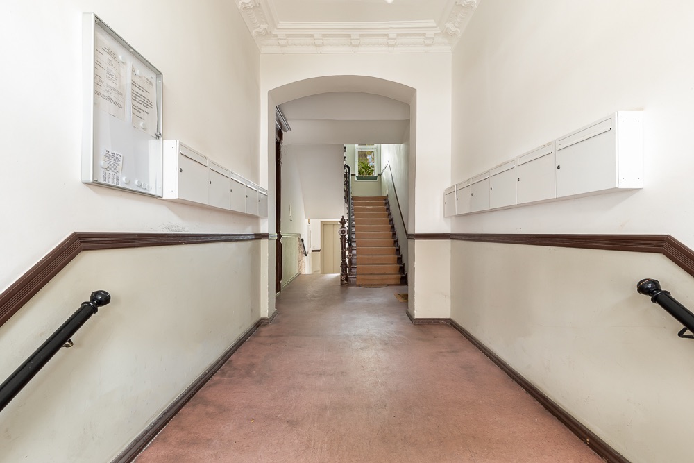 Flur eines Wohnhauses mit Briefkästen an den Wänden und Treppe im Hintergrund.