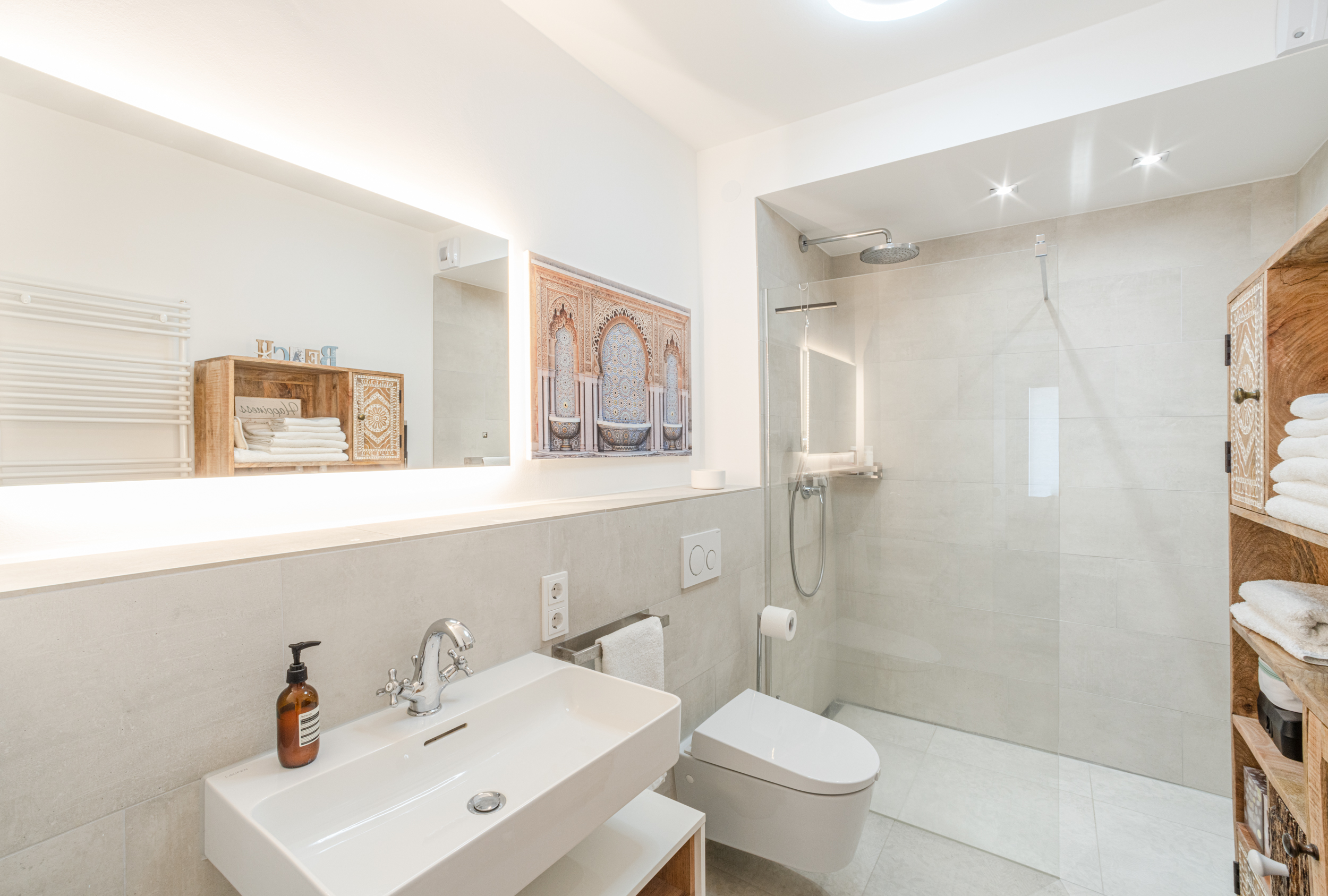 Helles, modernes Badezimmer mit Dusche, Waschbecken, WC und Regal mit Handtüchern.