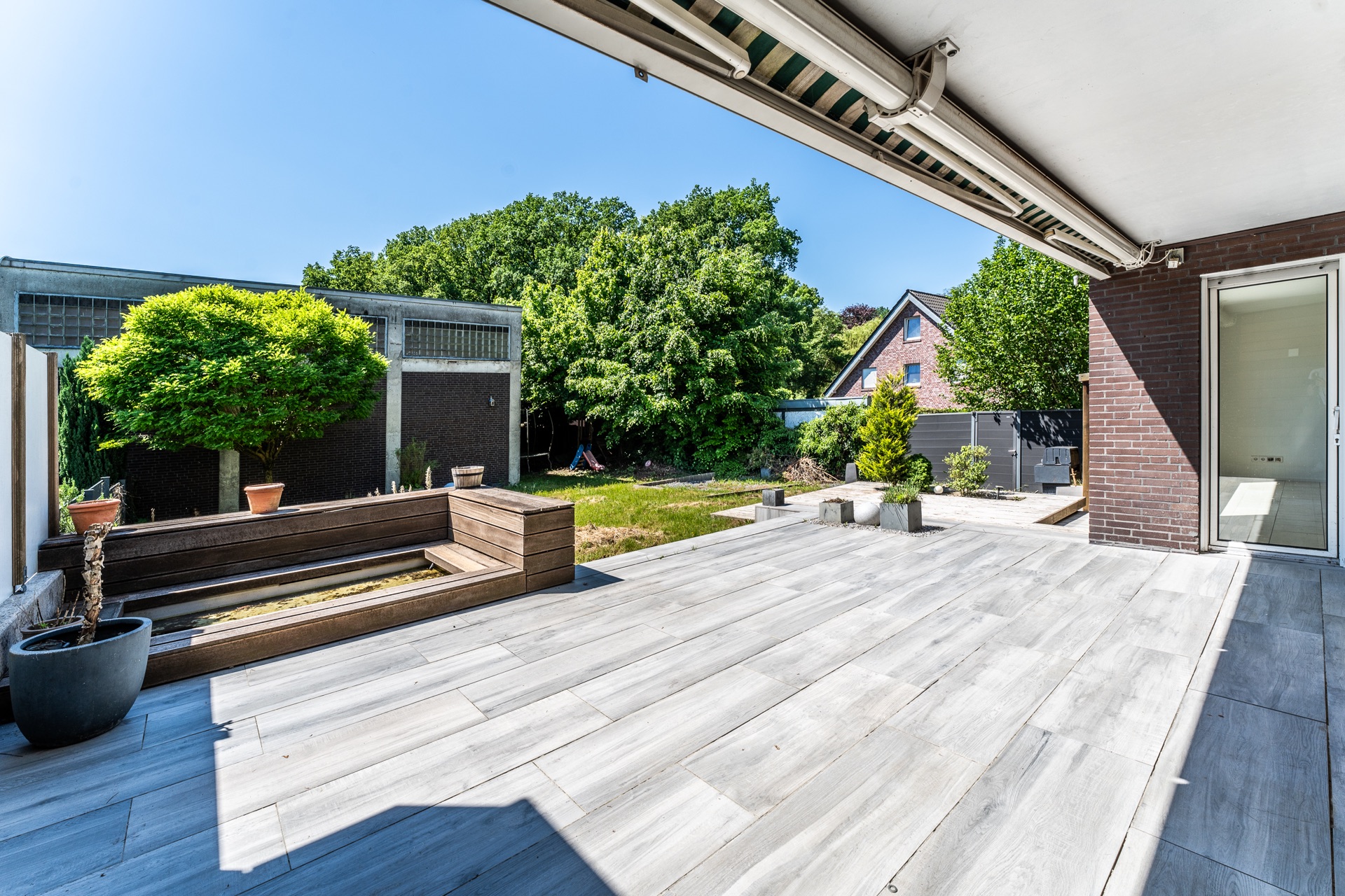 Große Terrasse mit Holzbänken, Pflanzkübeln und Blick auf Garten und Bäume.