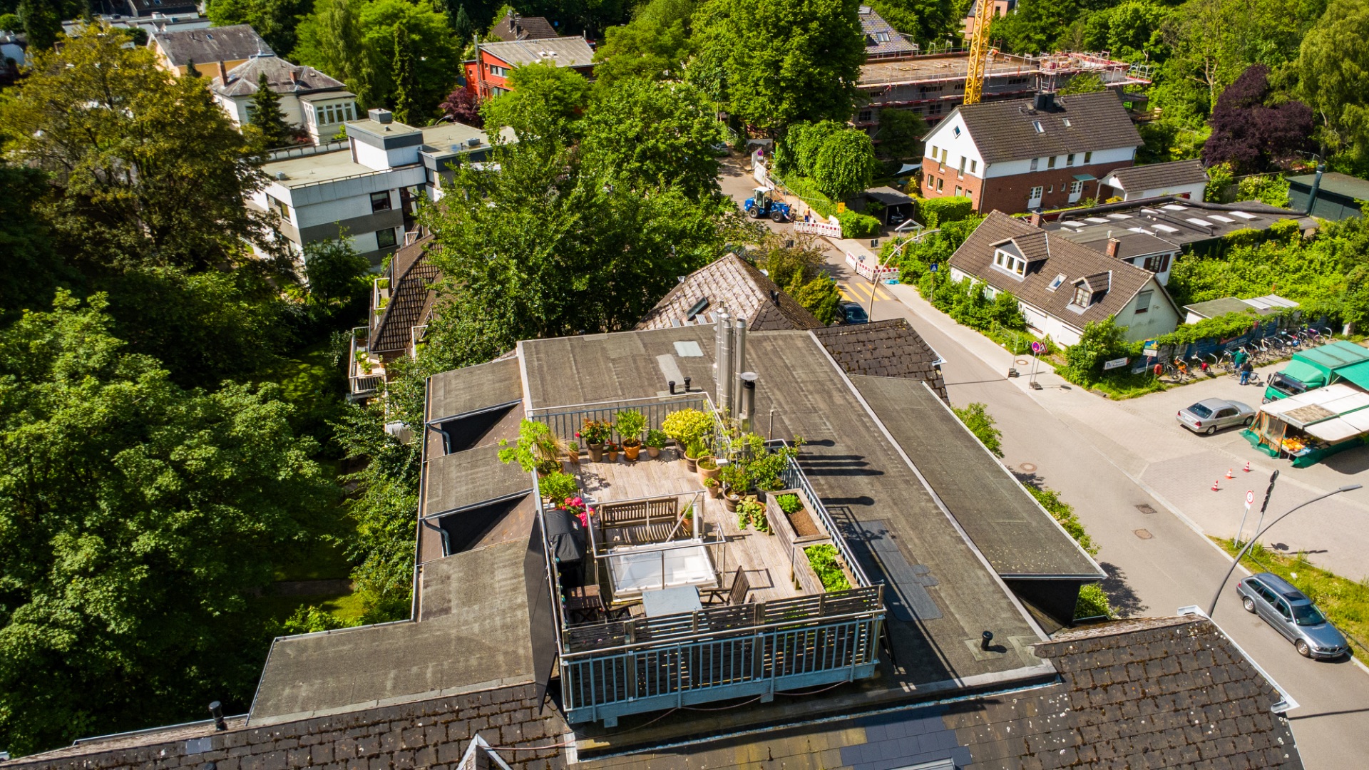 Dachterrasse mit Pflanzen und Sitzmöbeln auf einem Wohnhaus, von oben fotografiert.
