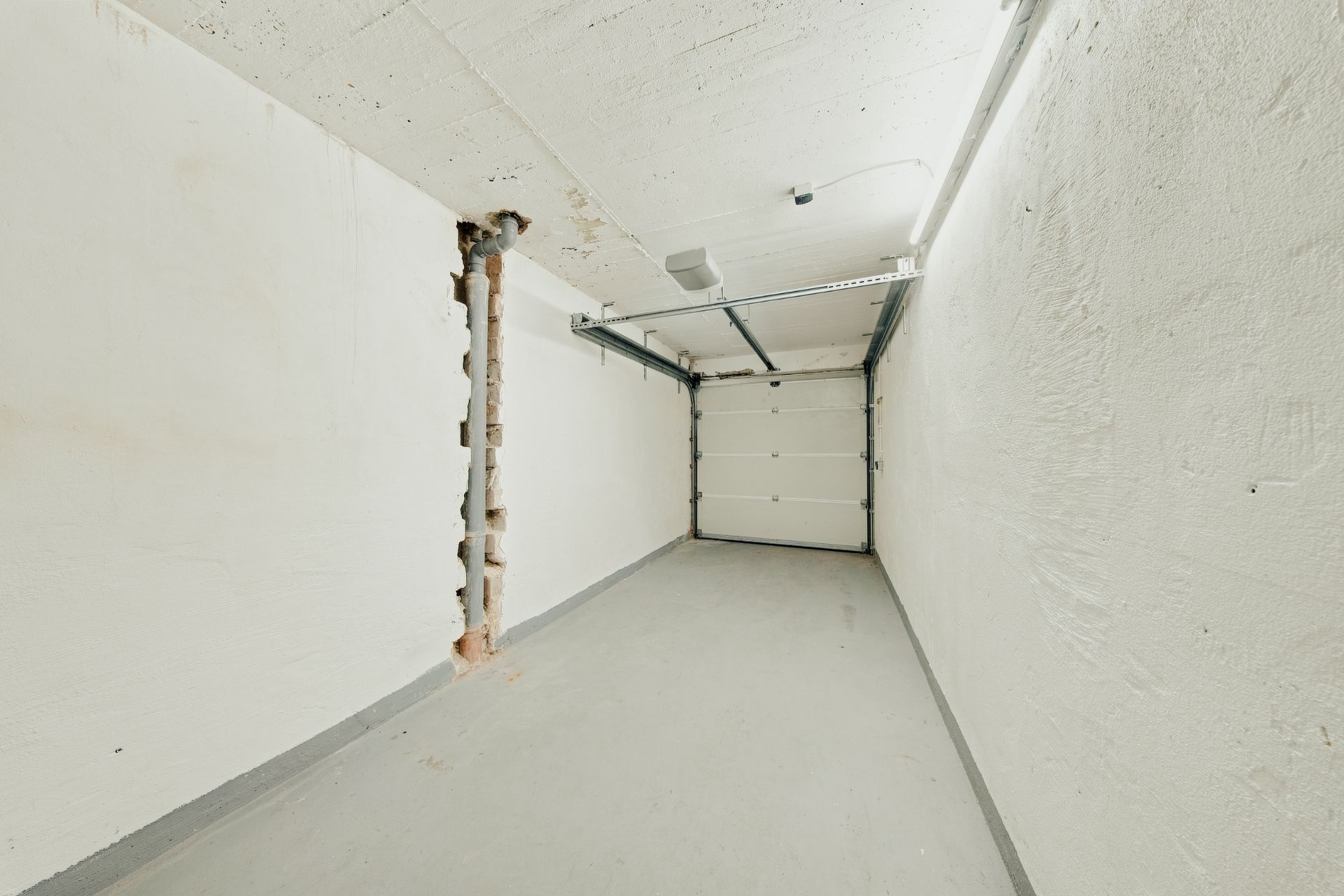 Leere, schmale Garage mit weiß gestrichenen Wänden und geschlossenem Garagentor.