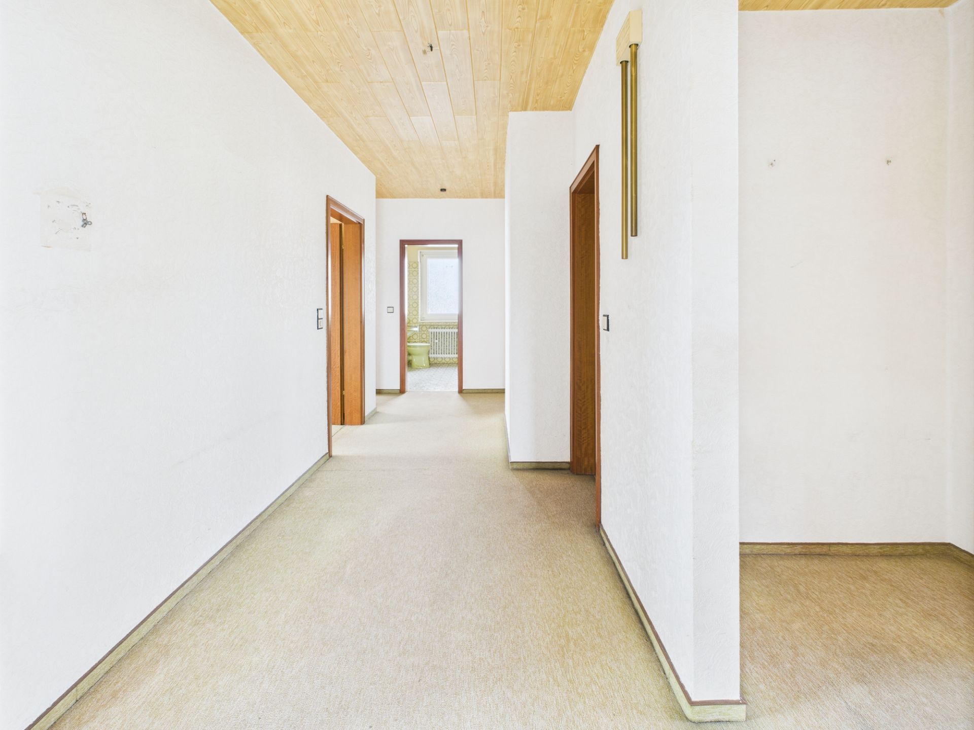 Heller Flur mit Holzboden, weißen Wänden und mehreren offenen Türen in einer Wohnung.
