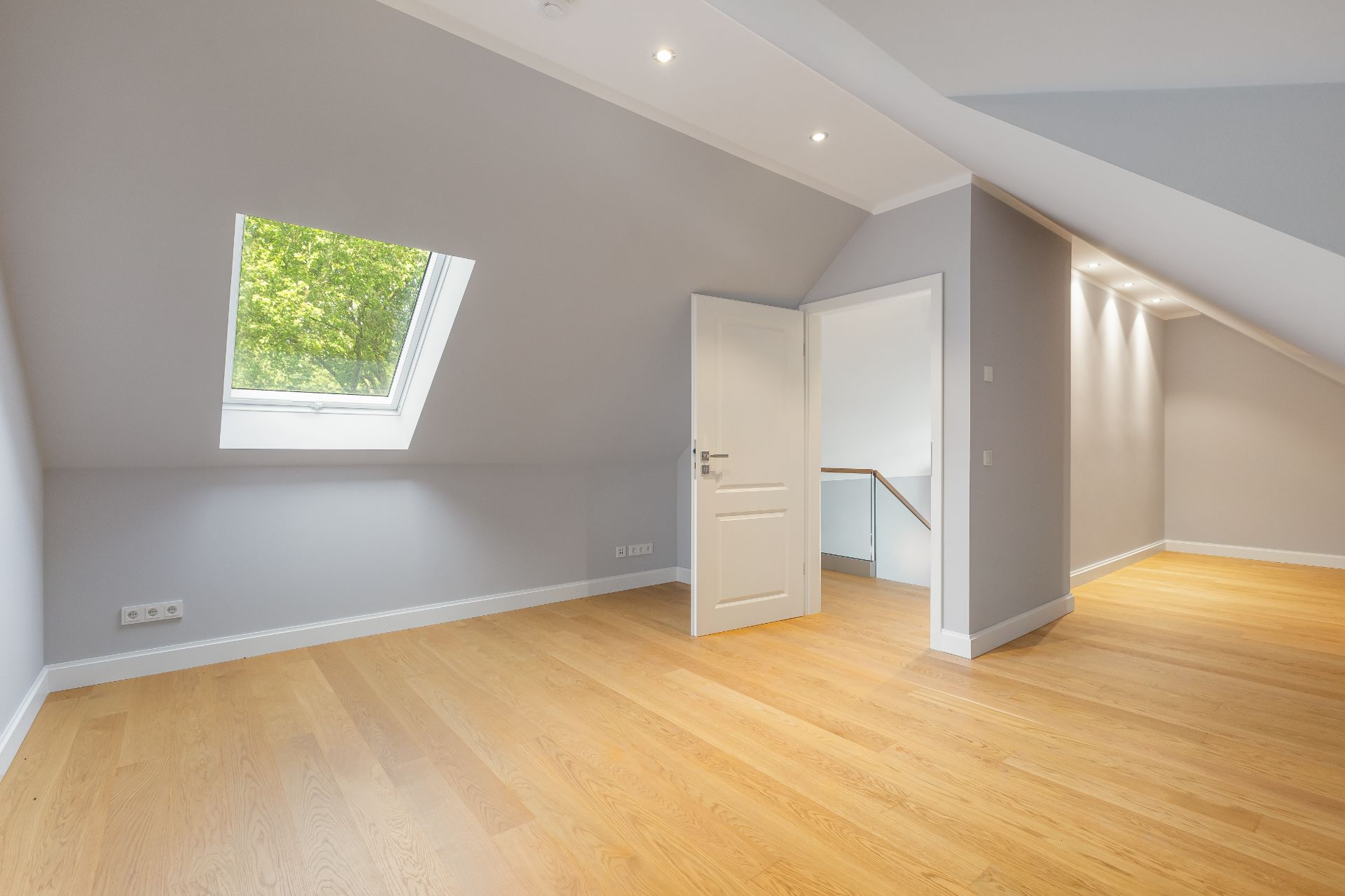 Heller Raum mit schräger Decke, Dachfenster, Holzboden und offener Tür.