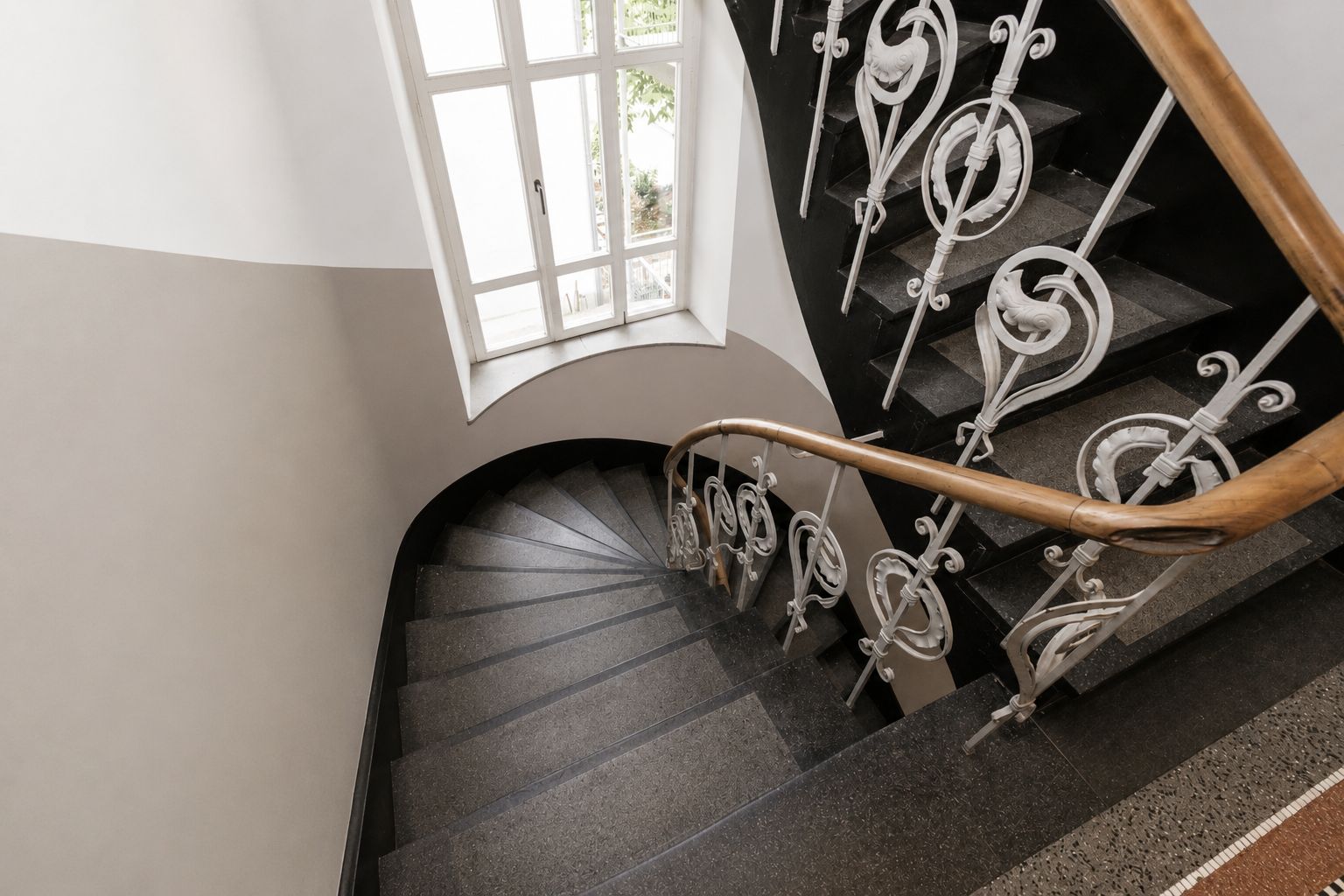 Treppe mit verziertem Geländer und Fenster im Treppenhaus eines Wohngebäudes.