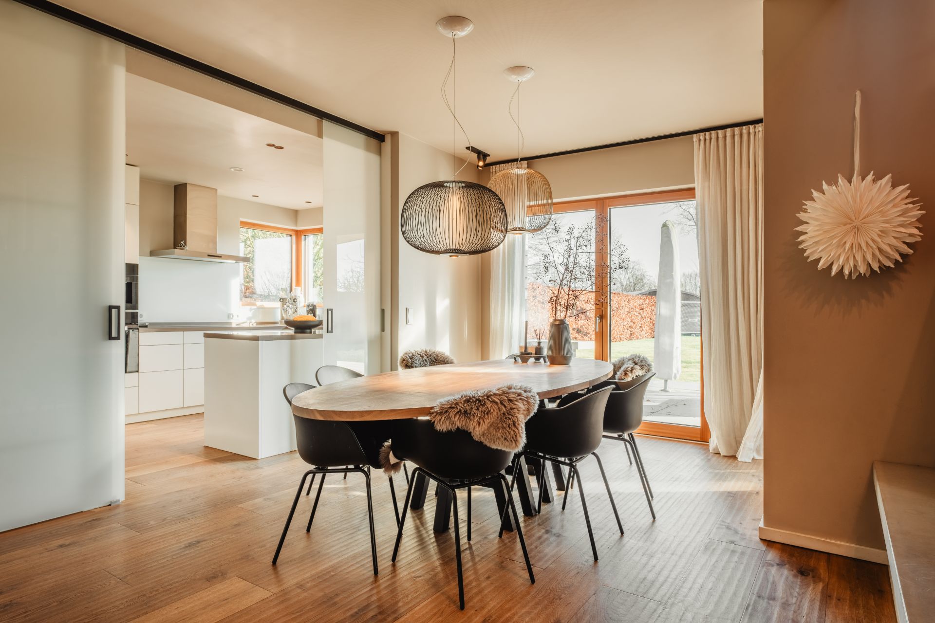 Heller Essbereich mit Holztisch, sechs Stühlen, großen Fenstern und Blick in die moderne Küche.