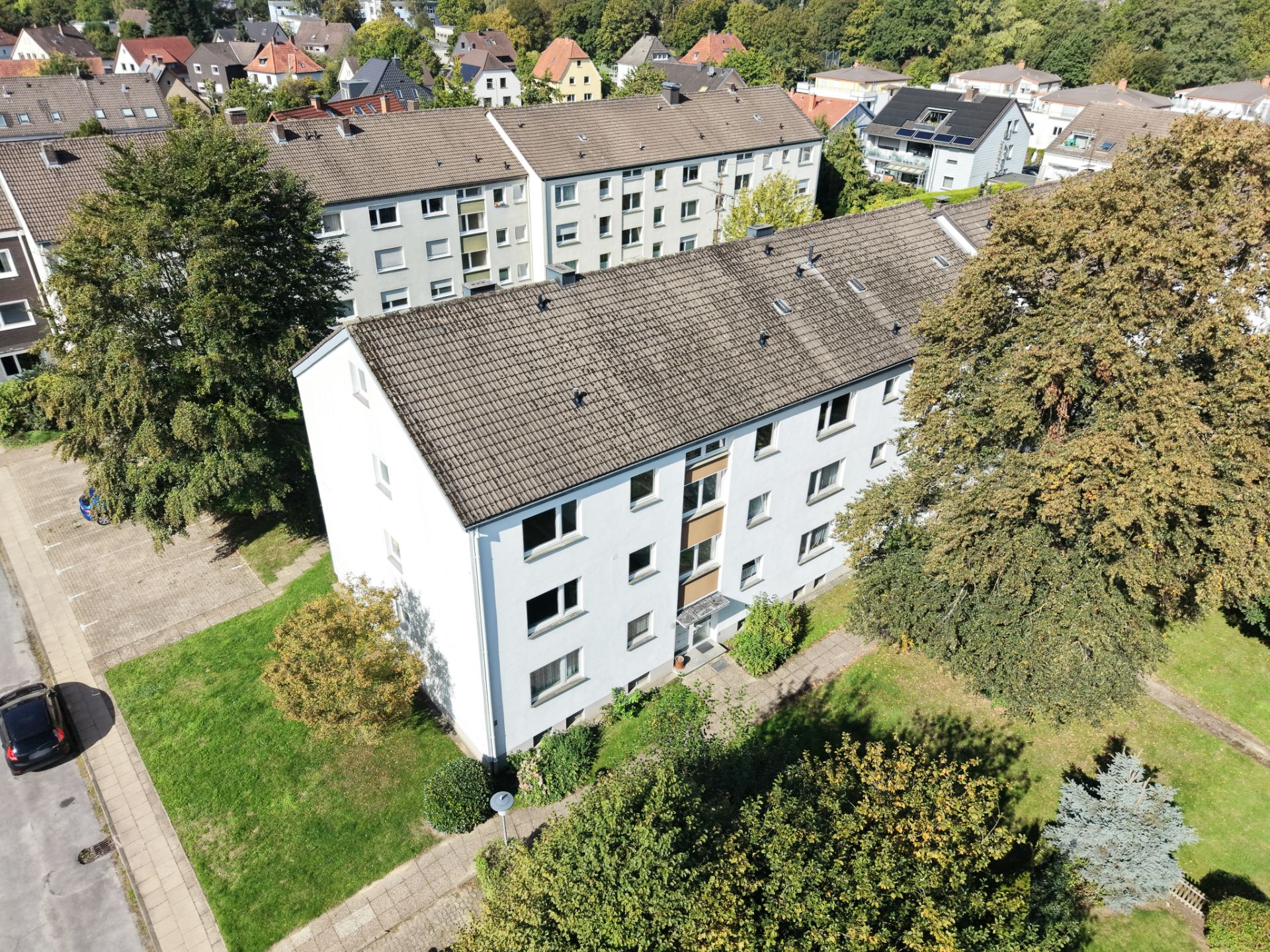 Mehrfamilienhaus mit weißer Fassade und Satteldach, umgeben von Bäumen und Gehwegen.