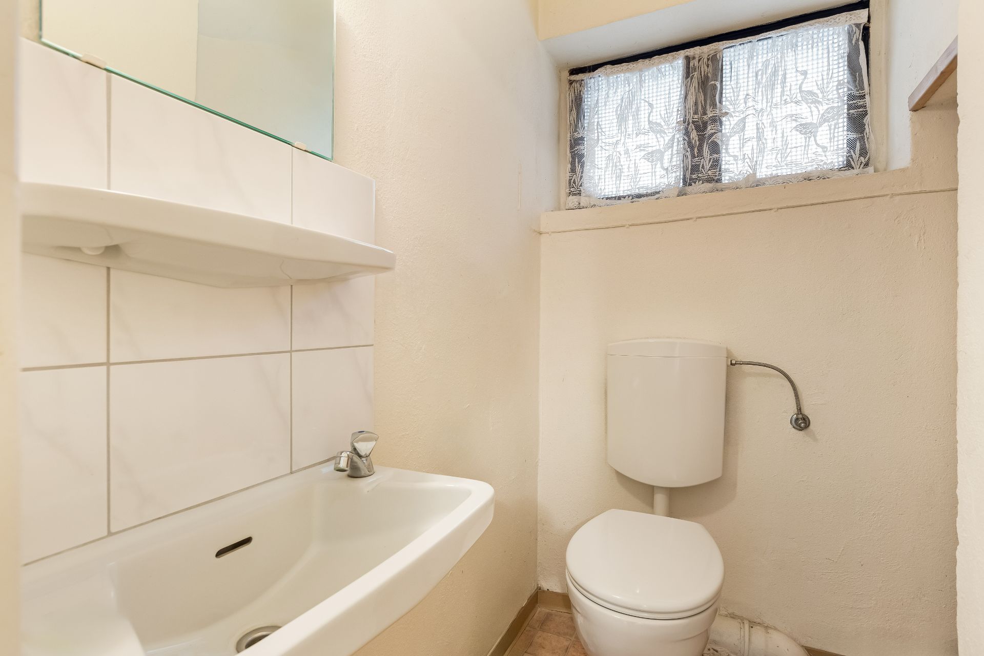 Kleines Badezimmer mit Waschbecken, WC und Fenster mit Vorhang.