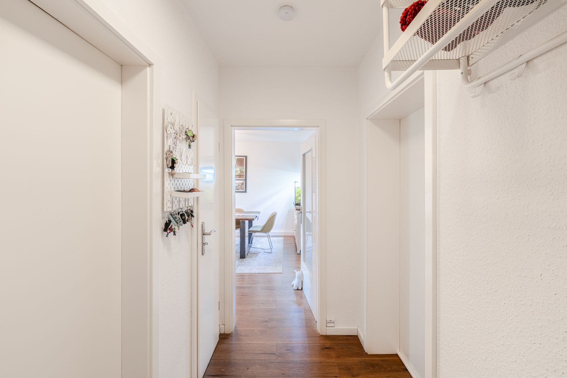 Heller Flur mit Holzboden, Garderobe, Schlüsselbrett und Blick in ein Esszimmer.