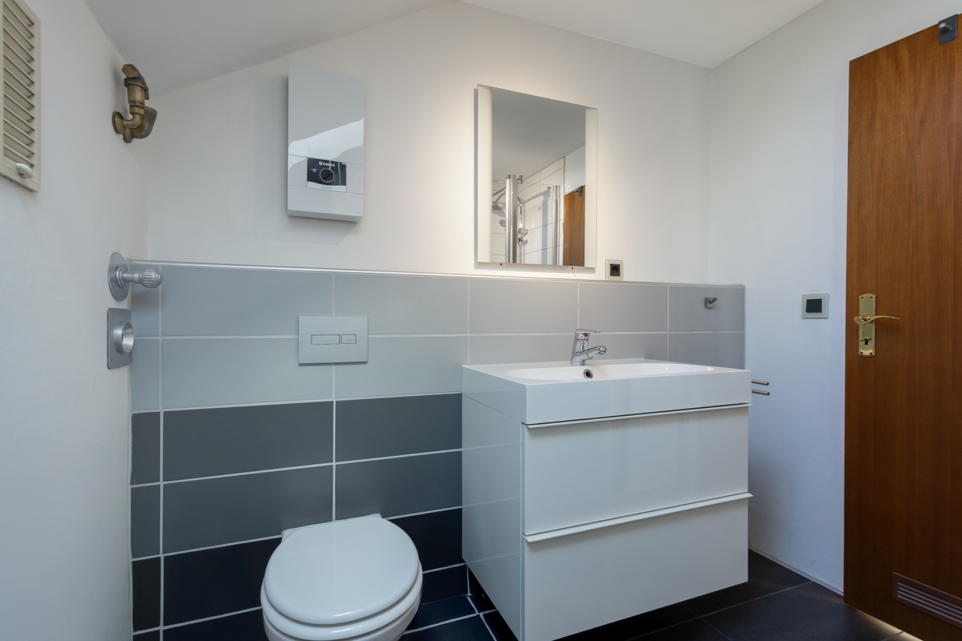 Modernes Badezimmer mit Waschbecken, Spiegel, Toilette und grauen Fliesen.