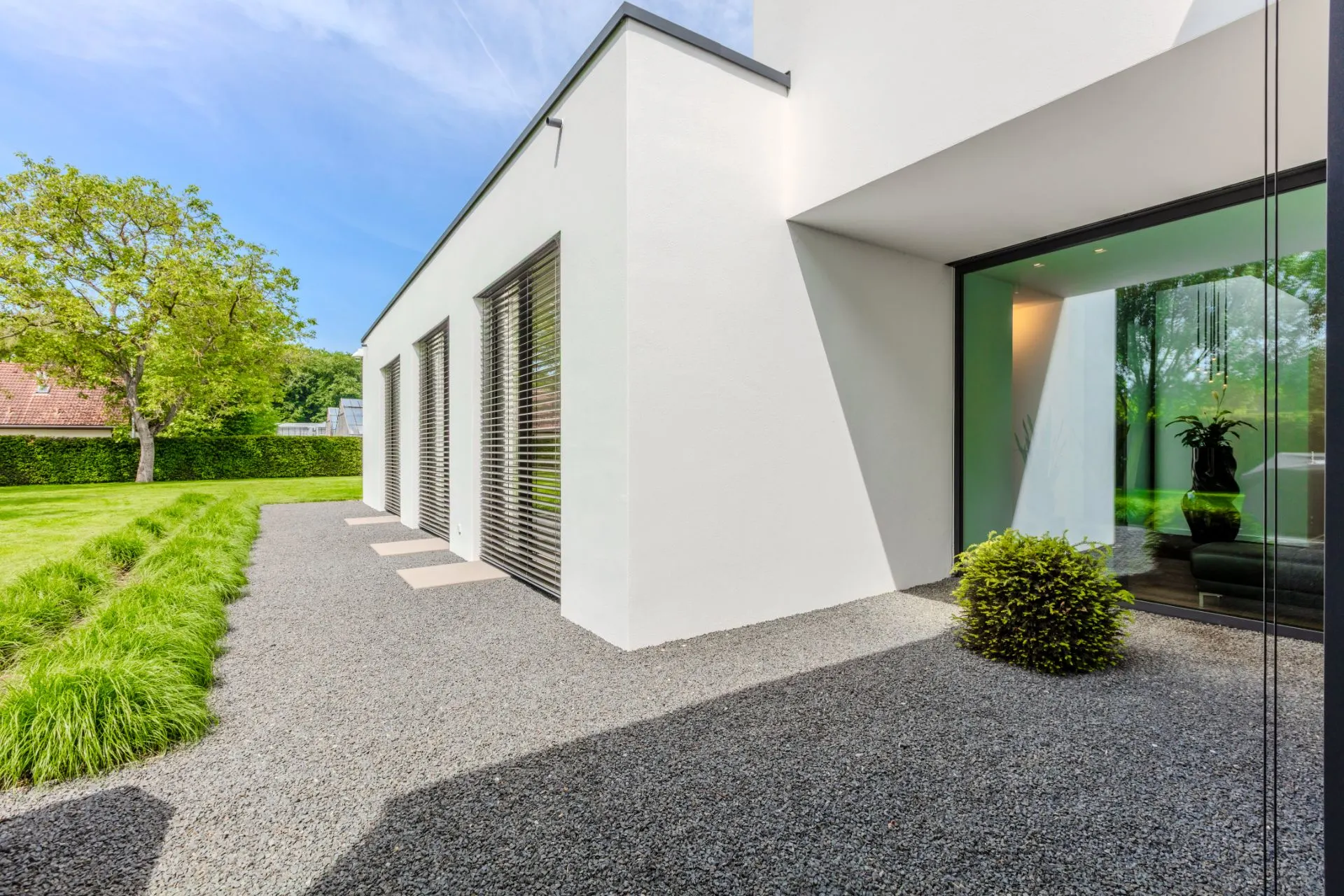Moderner weißer Hausaußenbereich mit großen Fenstern, Kiesweg und Rasen.