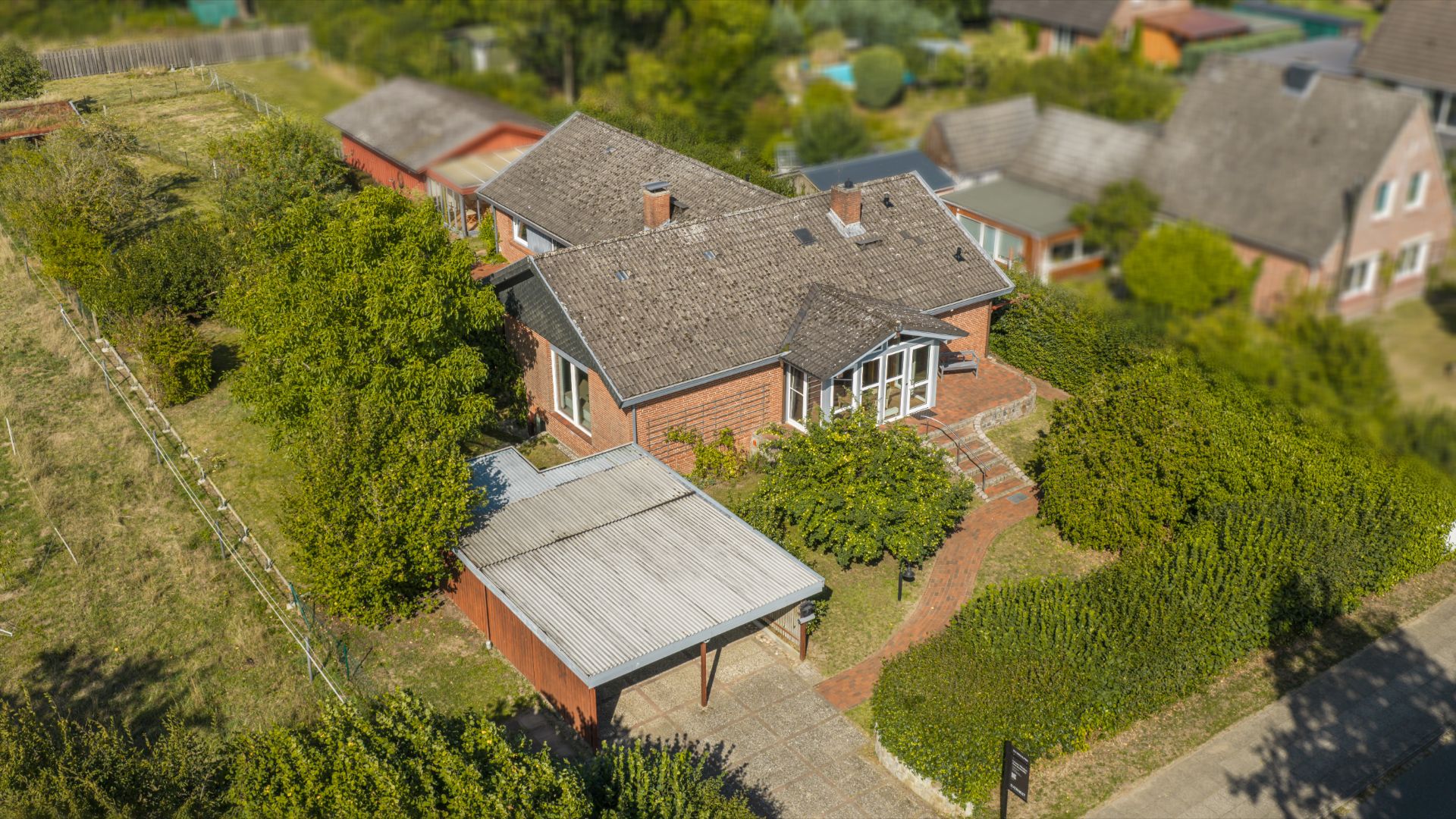 Luftaufnahme eines Einfamilienhauses mit Carport, Garten und umliegenden Häusern.