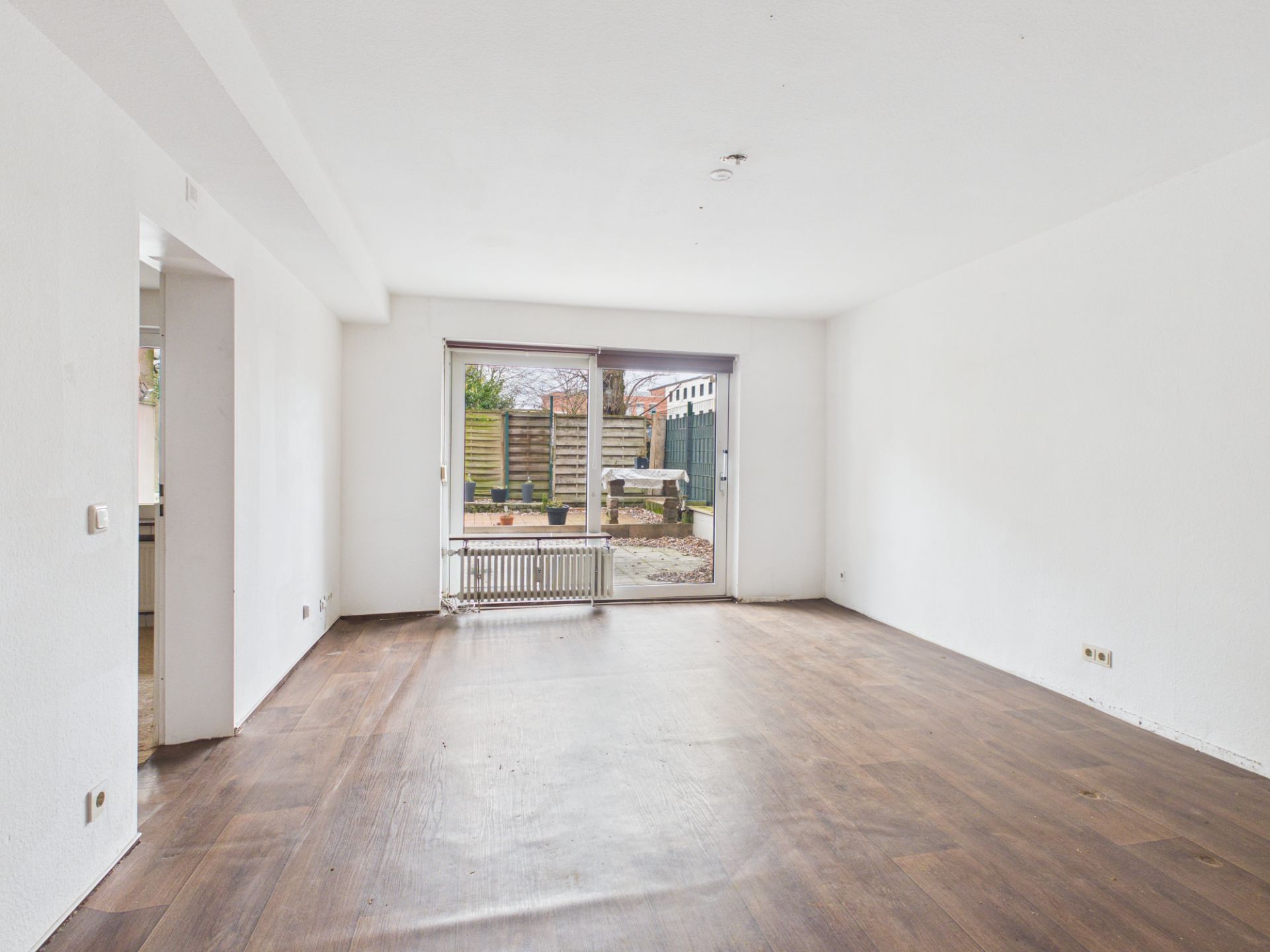 Leeres Wohnzimmer mit Holzfußboden und großer Fensterfront zum Garten.