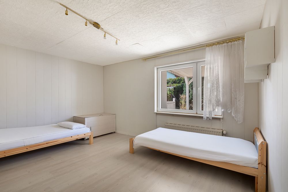 Helles Schlafzimmer mit zwei Einzelbetten, Fenster, Vorhängen und einer Kommode.