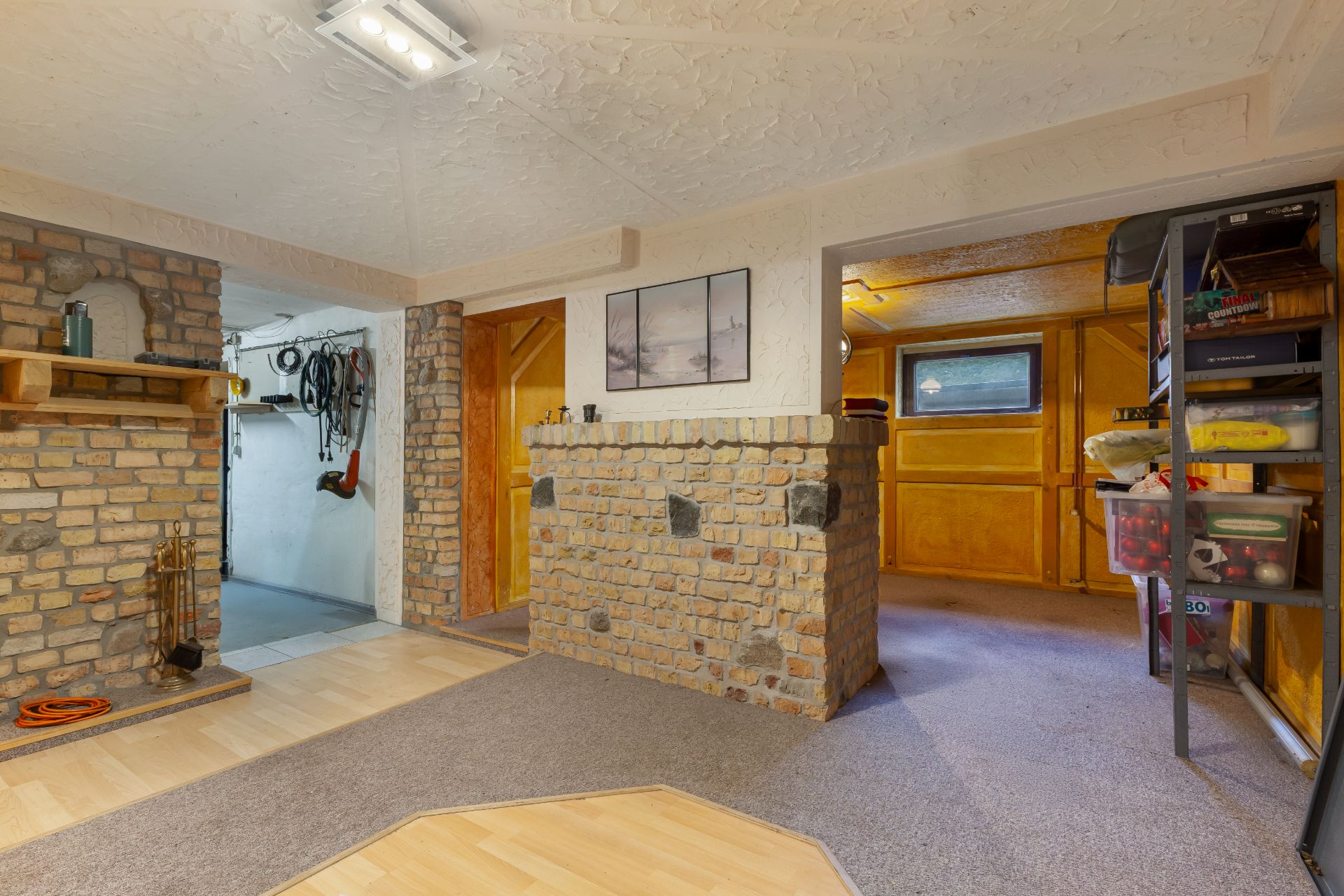 Kellerraum mit gemauerter Wand, Regal, Kamin und Blick in einen weiteren Raum.