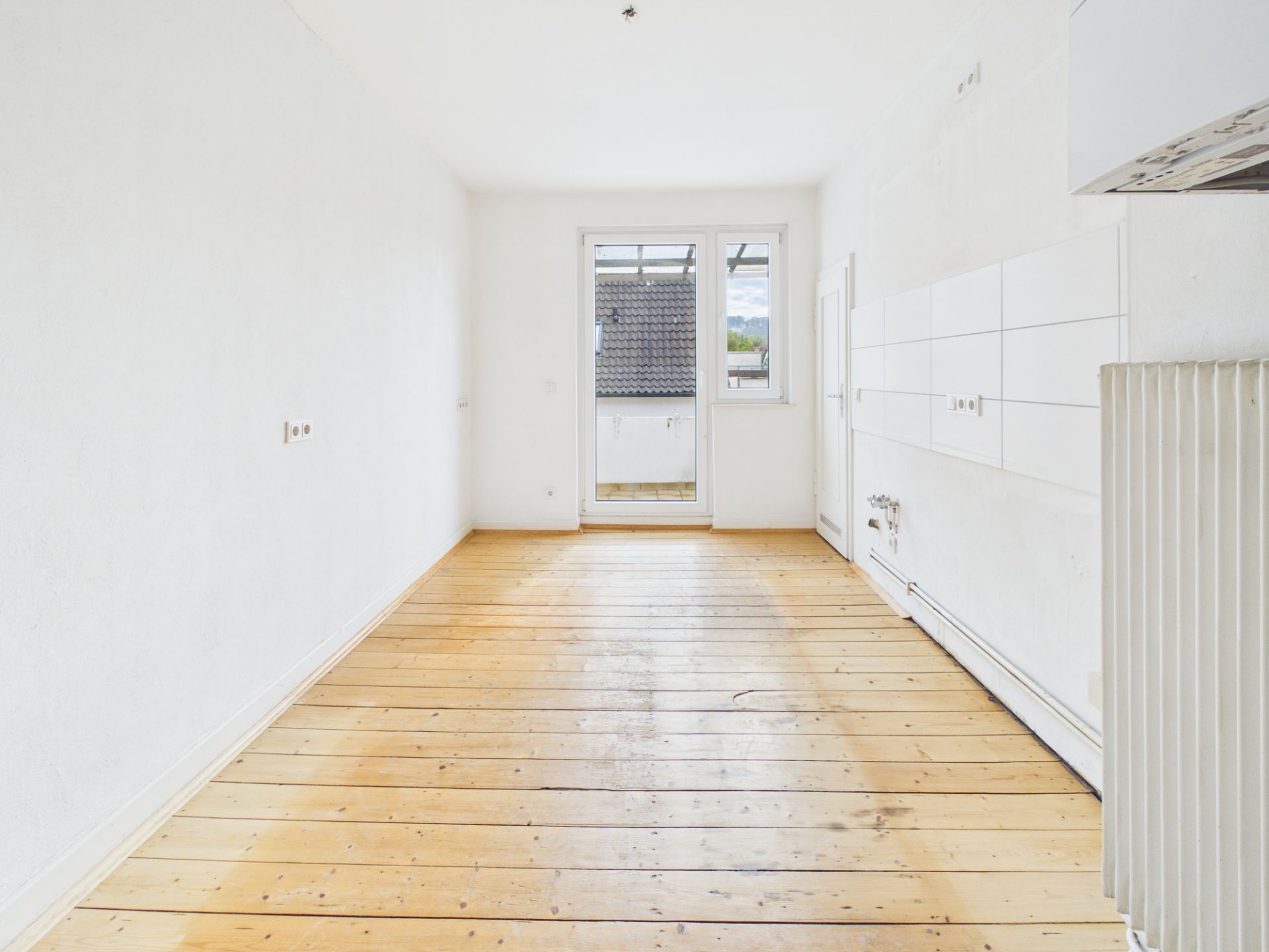 Leerer Raum mit Holzboden, weißen Wänden und Balkontür.