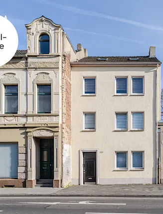 Zwei nebeneinanderstehende Wohnhäuser und ein flaches Gebäude an einer Straße bei Tageslicht.