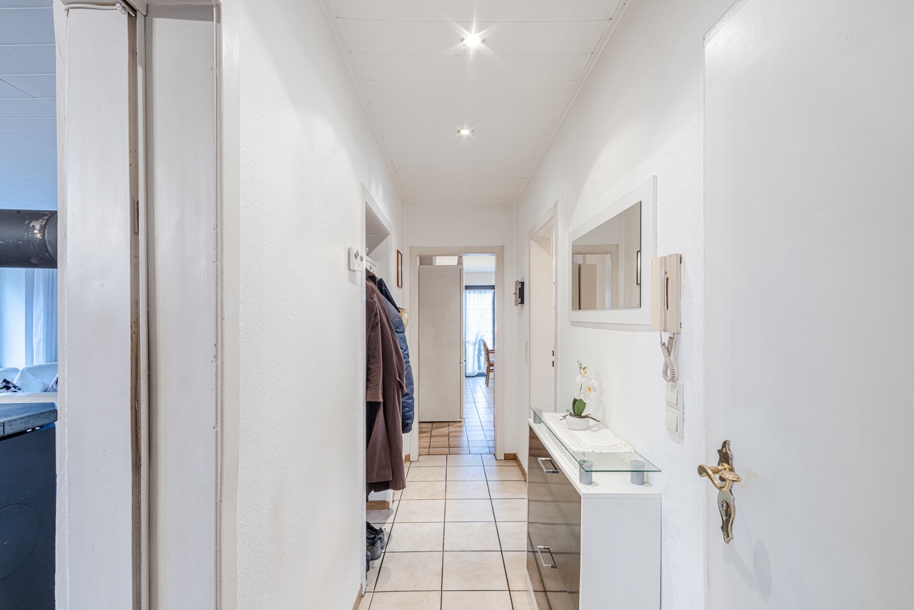 Heller Flur mit Fliesenboden, Garderobe, Spiegel und Kommode mit Blume.
