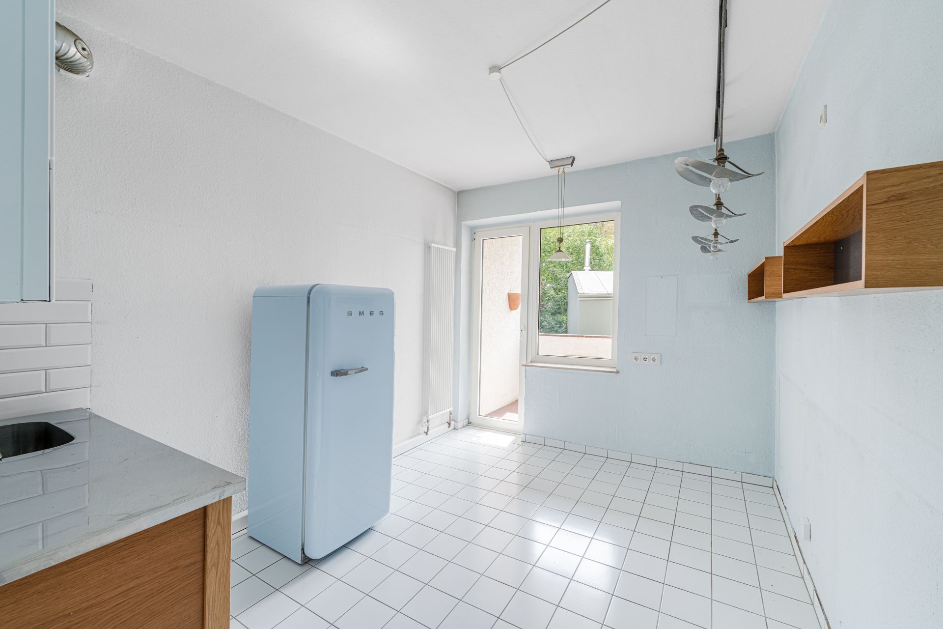 Helle Küche mit weißem Fliesenboden, blauem Kühlschrank und Holzwandregalen.