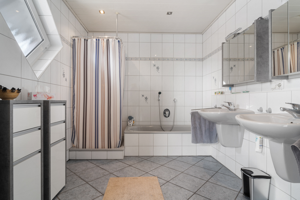 Helles Badezimmer mit Badewanne, Duschvorhang, Doppelwaschbecken und zwei Spiegelschränken.