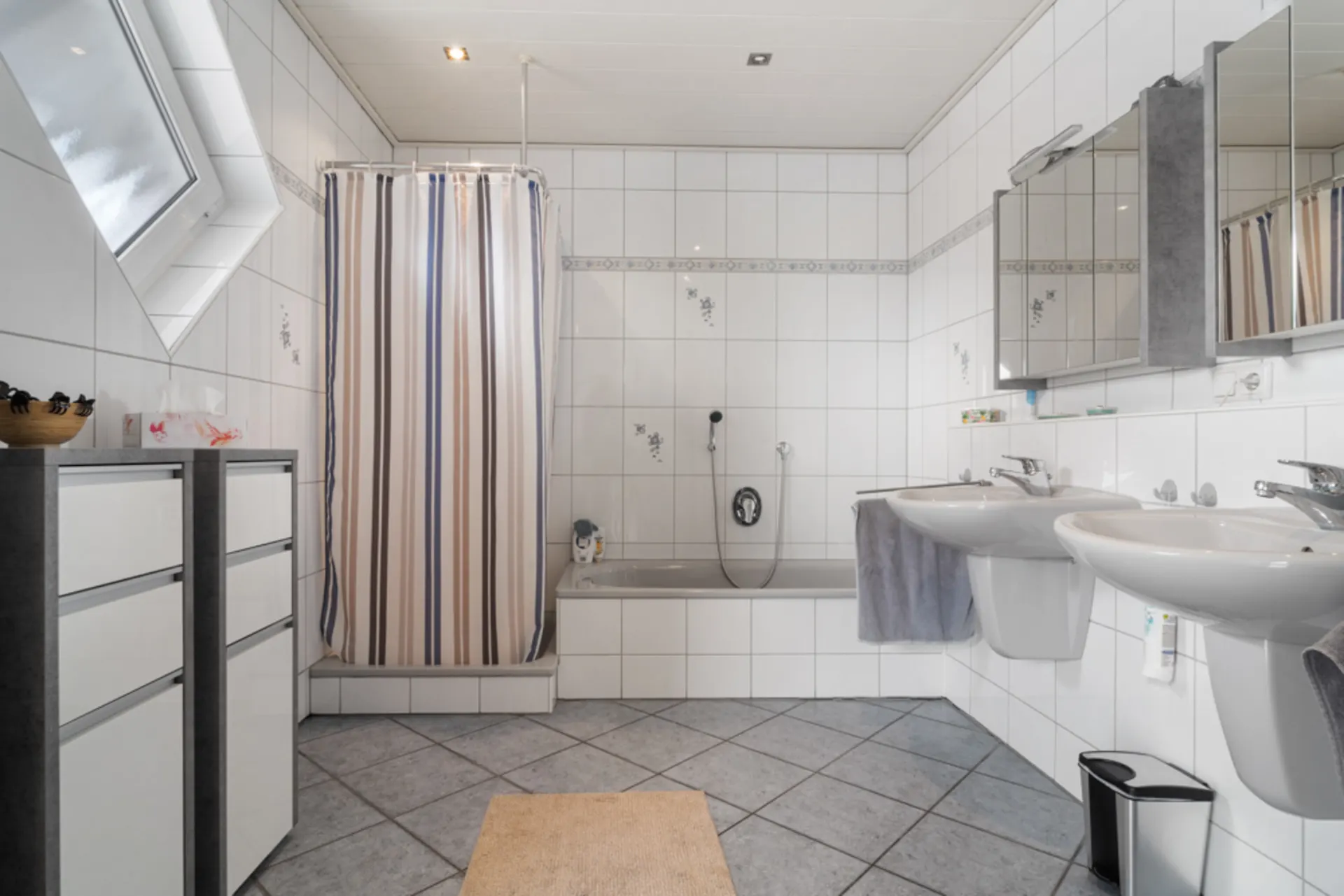 Helles Badezimmer mit Badewanne, Duschvorhang, Doppelwaschbecken und zwei Spiegelschränken.
