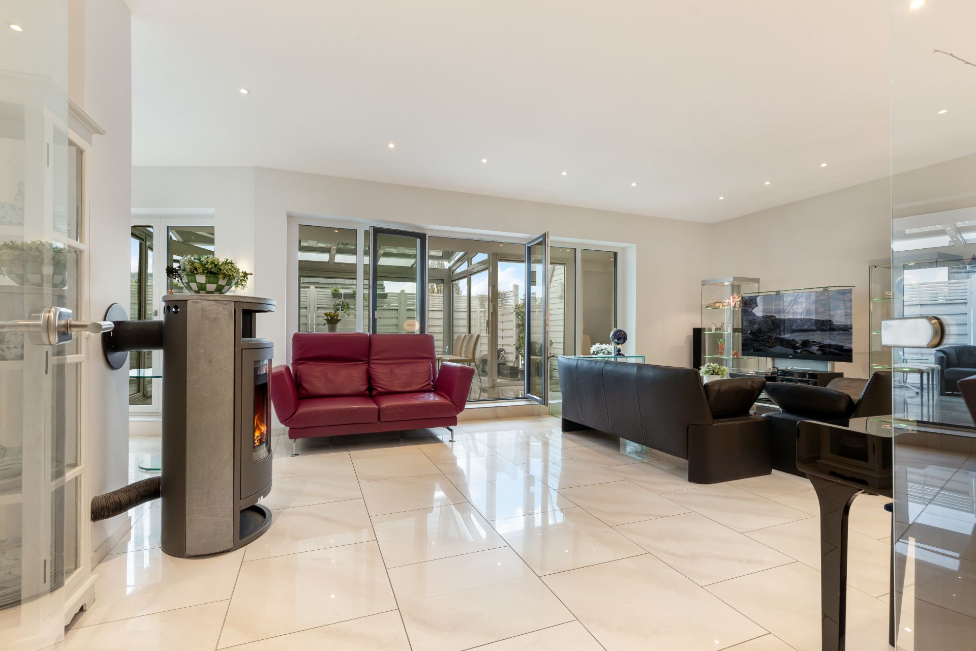 Modernes Wohnzimmer mit Kamin, roten und schwarzen Sofas, Fernseher und großen Fenstern zum Wintergarten.