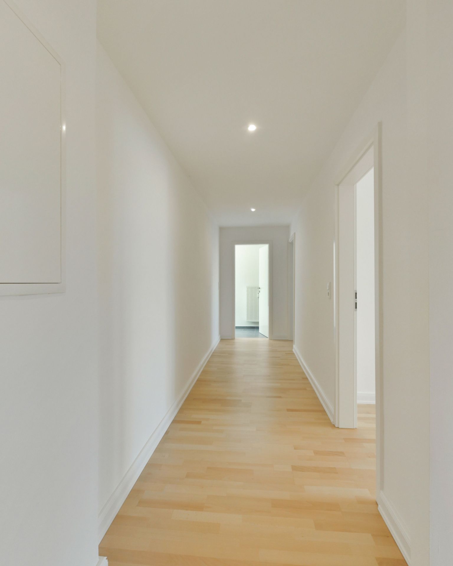 Heller Flur mit Holzfußboden und weißen Wänden in einer Wohnung.