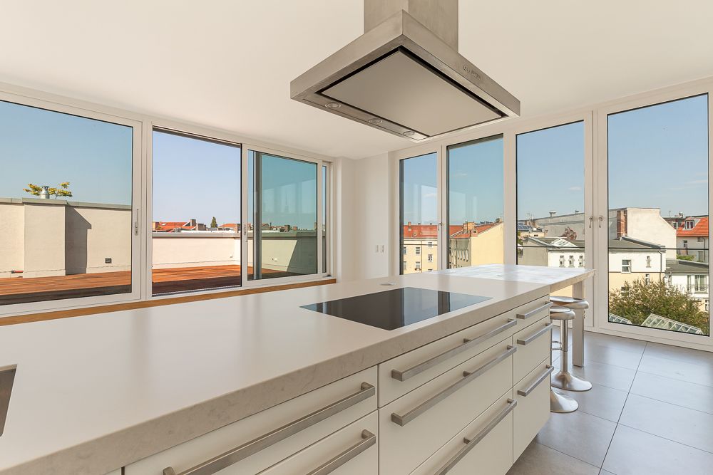 Moderne Küche mit Kochinsel, großen Fenstern und Blick auf Dachterrasse und Stadt.