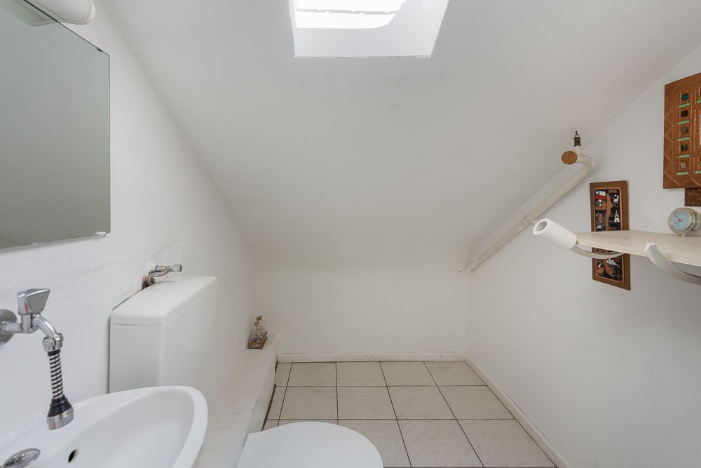 Kleines Badezimmer mit weißer Wand, Dachfenster, Toilette und Waschbecken unter der Schräge.