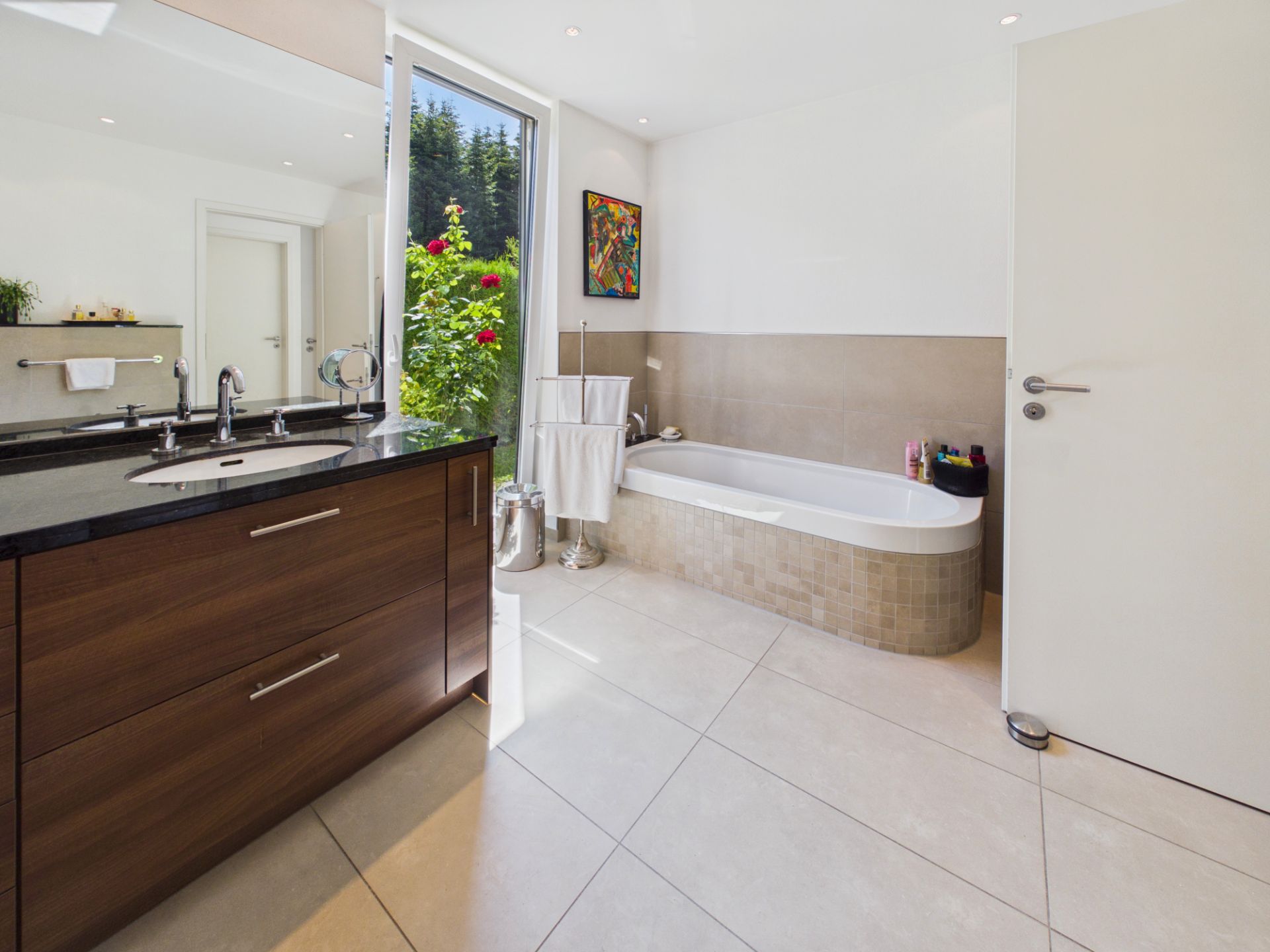 Modernes Badezimmer mit Badewanne, Doppelwaschbecken und Fenster mit Blick ins Grüne.