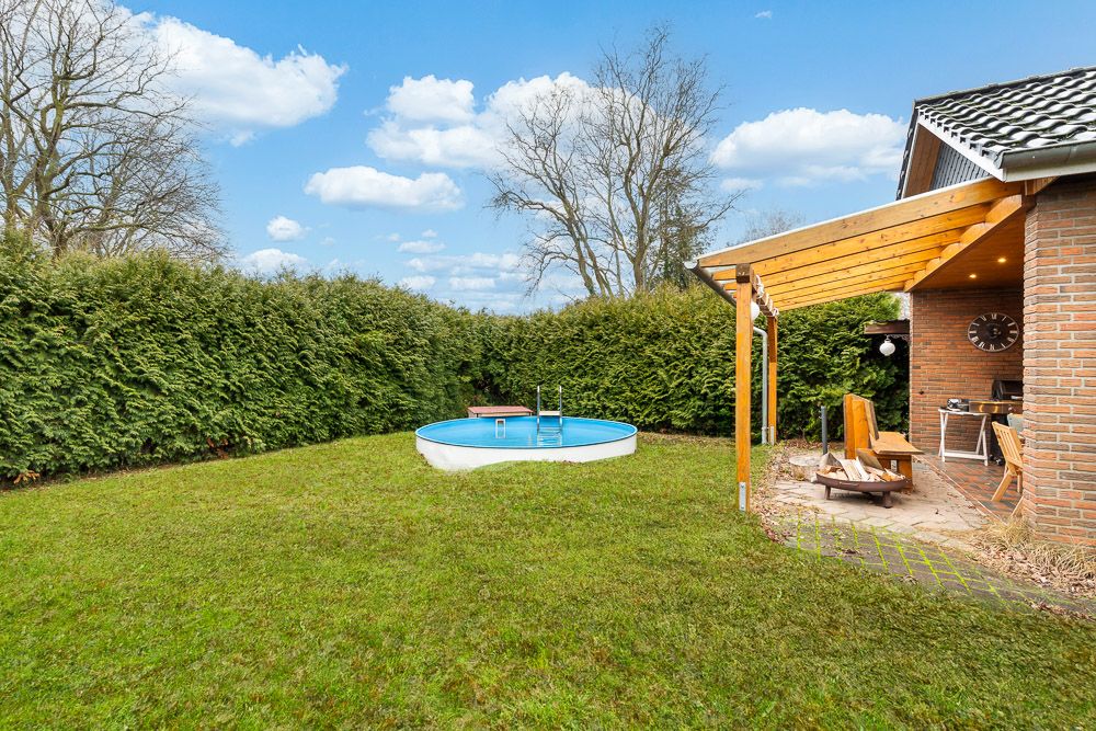 Grüner Garten mit kleinem Rundpool und überdachter Terrasse an einem Backsteinhaus.