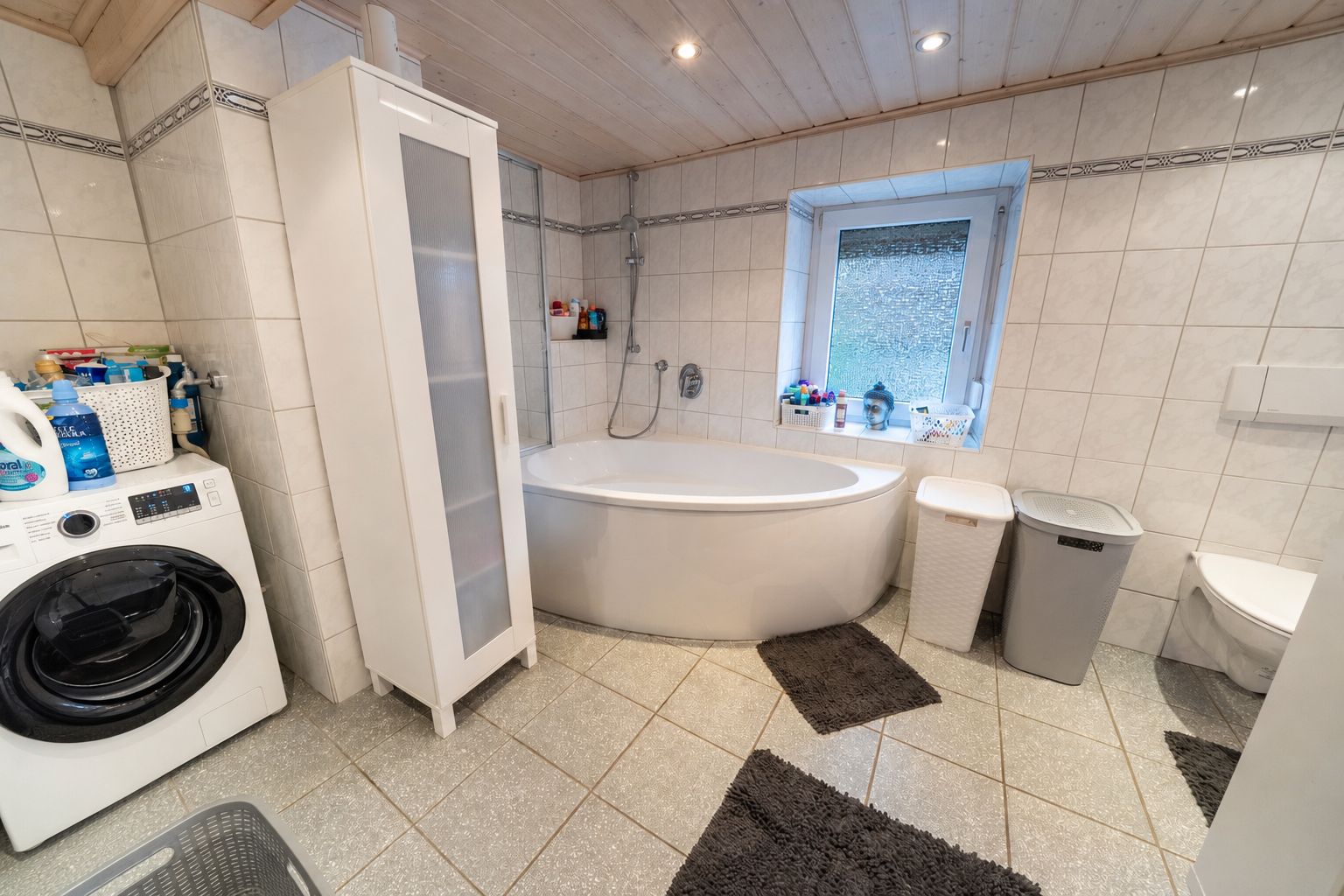 Modernes Badezimmer mit Eckbadewanne, Waschmaschine, Schrank und Fenster.